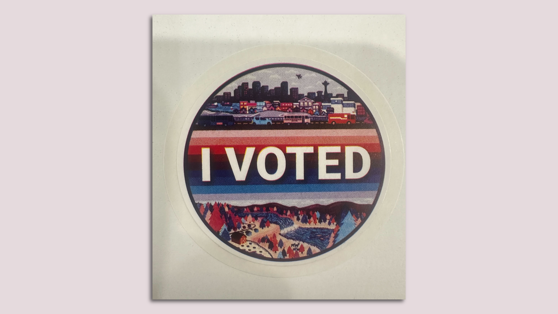 A photo of King County's "I voted" sticker, which features a Seattle cityscape illustration and a view of a rural landscape that includes Snoqualmie Falls.