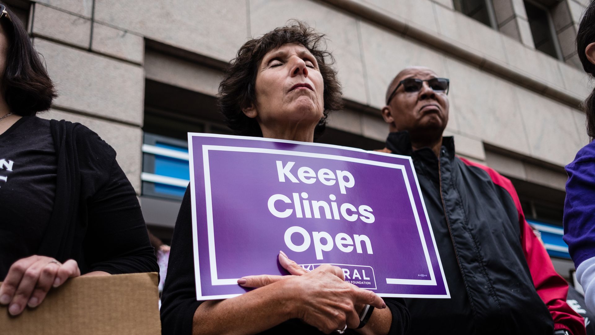 Photo of a protester holding a sign that says "Keep clinics open" 