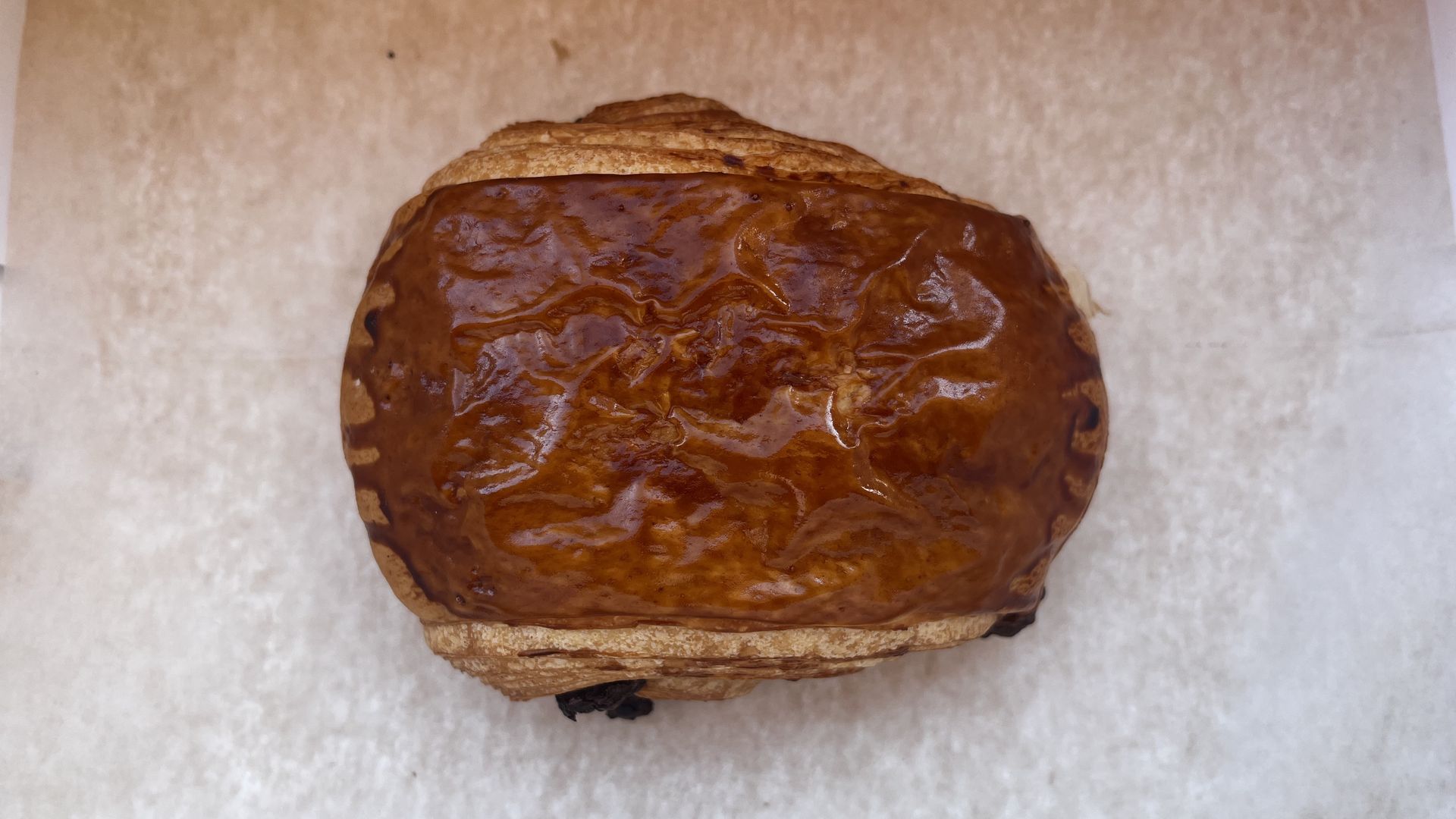 Top-down view of a glossy, caramel-brown loaf on parchment paper. The rectangular bread has a dark golden crust with a slight sheen.