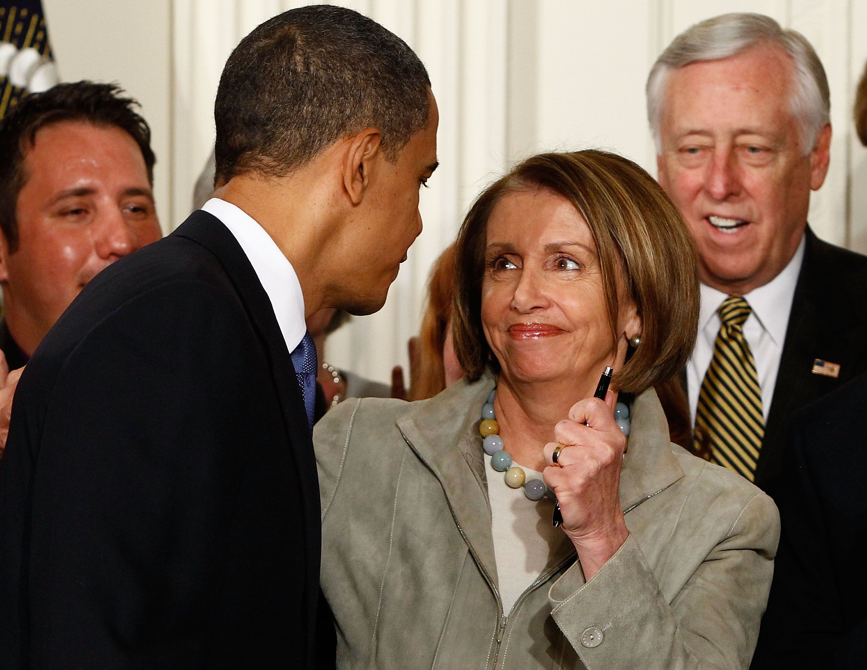 Nancy Pelosi holds a pen from the ACA signing ceremony alongside Steny Hoyer and other officials in the East Room of the White House.