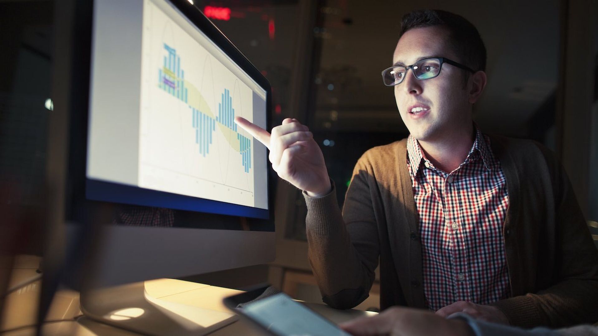 A man wearing glasses points to blue bar graphs on a computer screen. 