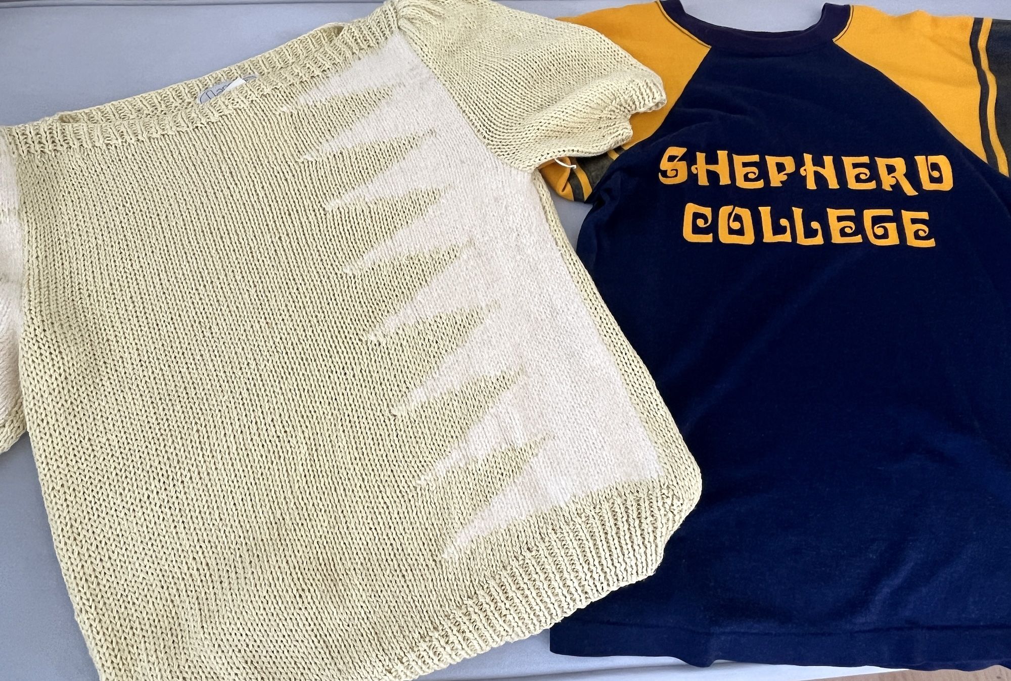 A yellow short sleeve sweater with white triangles and blue and gold ringer tee that reads Shepherd College.