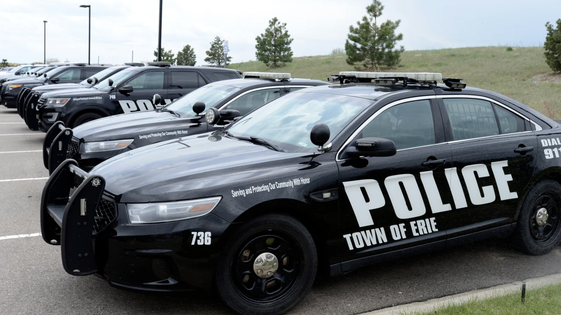 Row of black police cars marked "POLICE TOWN OF ERIE" parked in a lot on a cloudy day, with light bars and push bumpers visible.