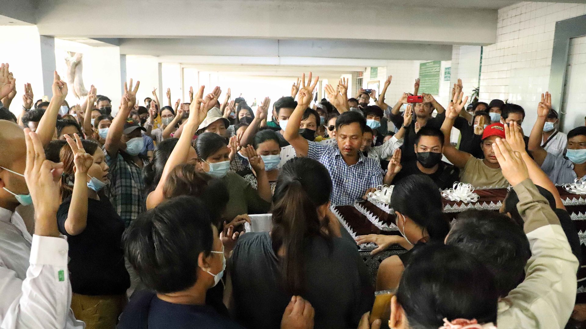 Photo of people holding three fingers up as they surround a coffin