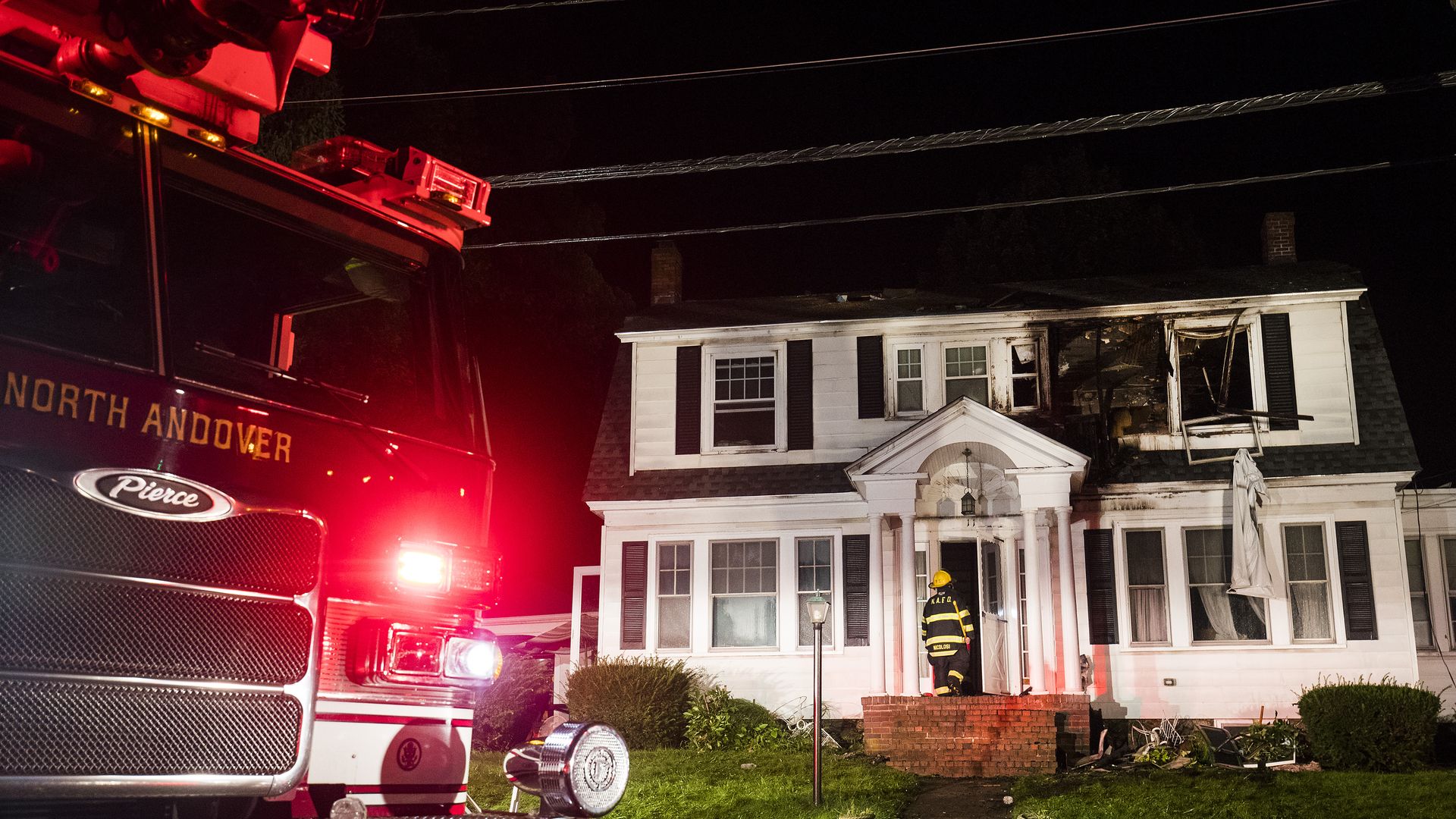 Photo of house north of Boston that has exploded and burned window with firefighters outside it