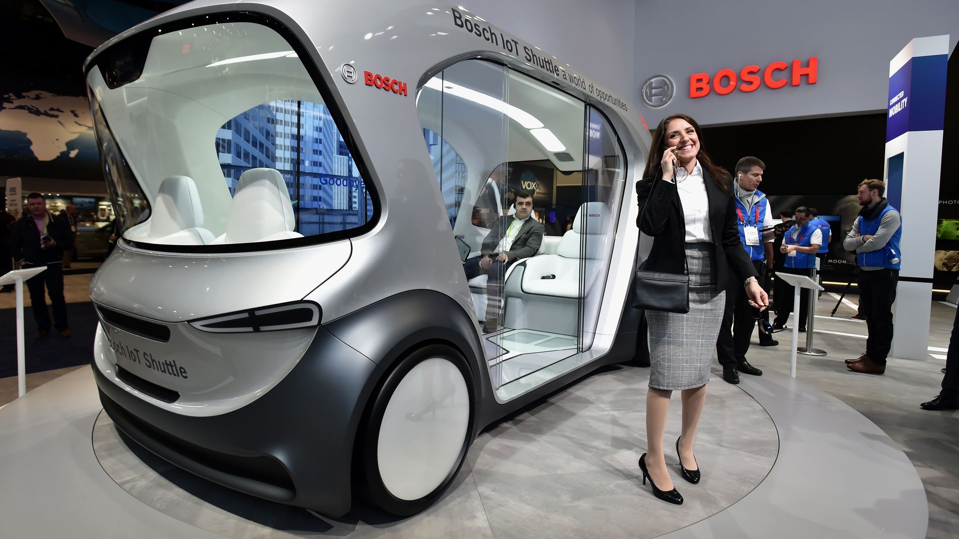 A woman stands near a Bosch automatous shuttle on display at CES