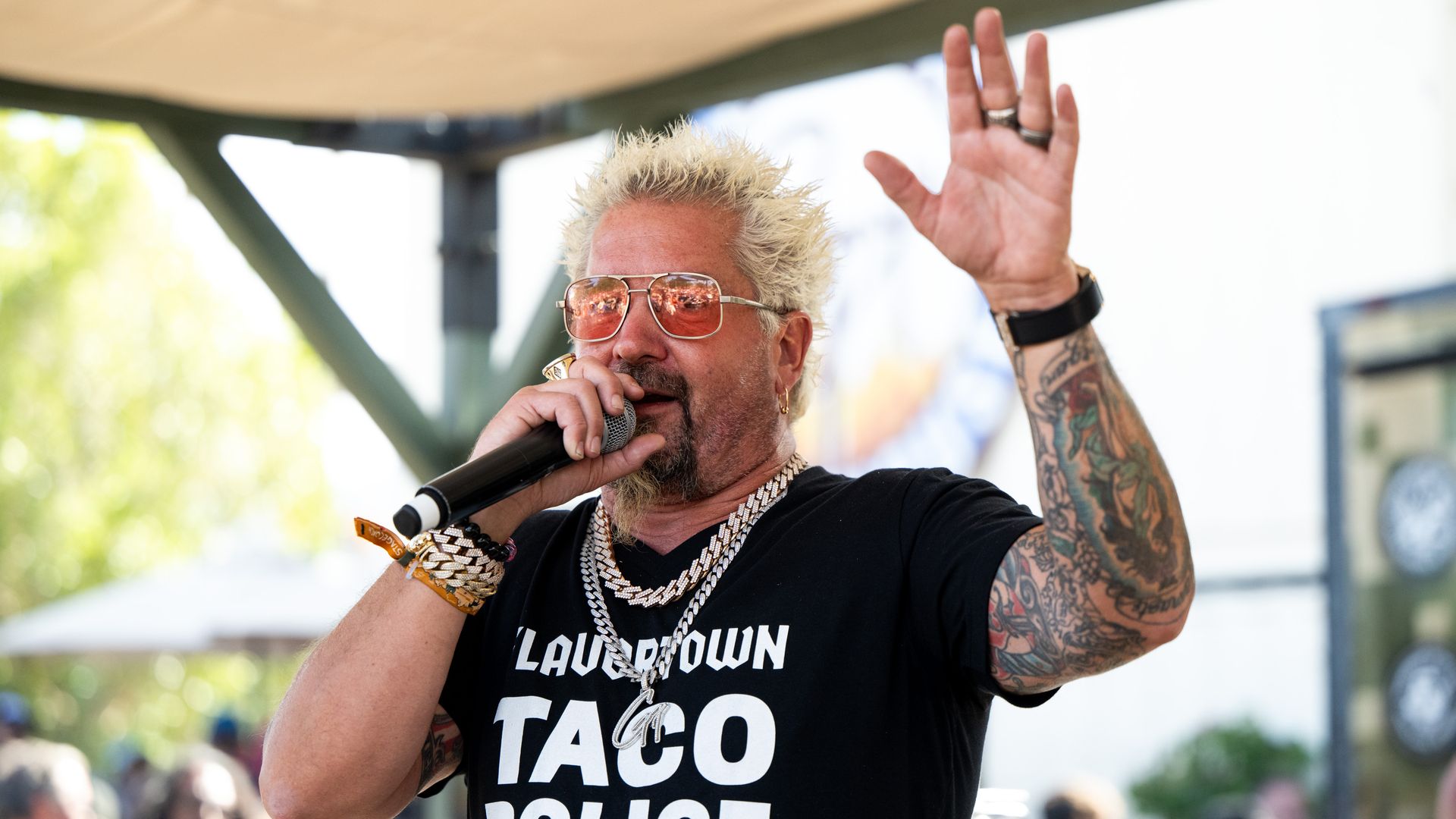 Celebrity chef Guy Fieri talks into a microphone with his hand raised