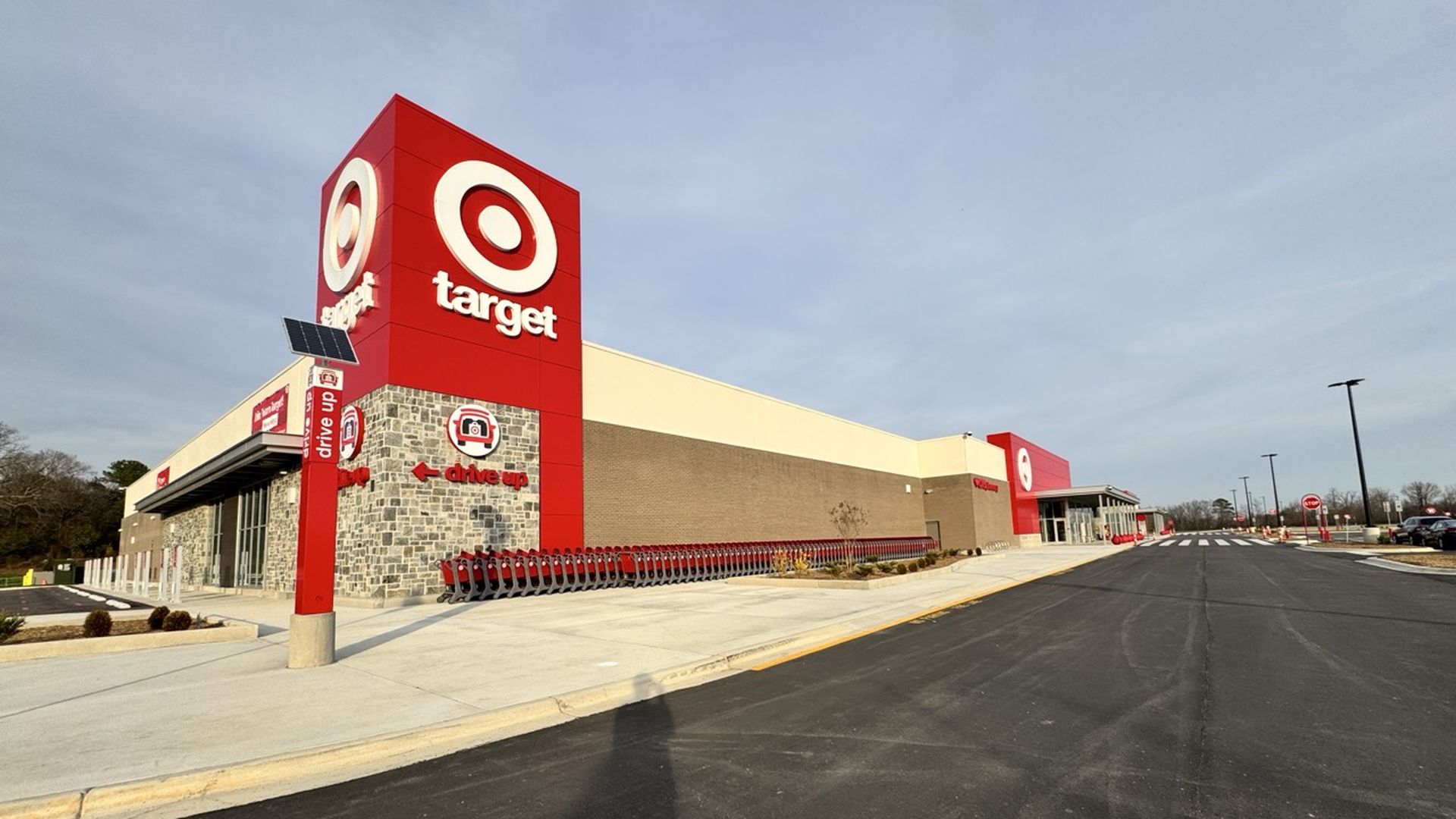 Exterior view of a Target store with the red and white Target logo on a tall sign and building, lined with shopping carts on a clear day.