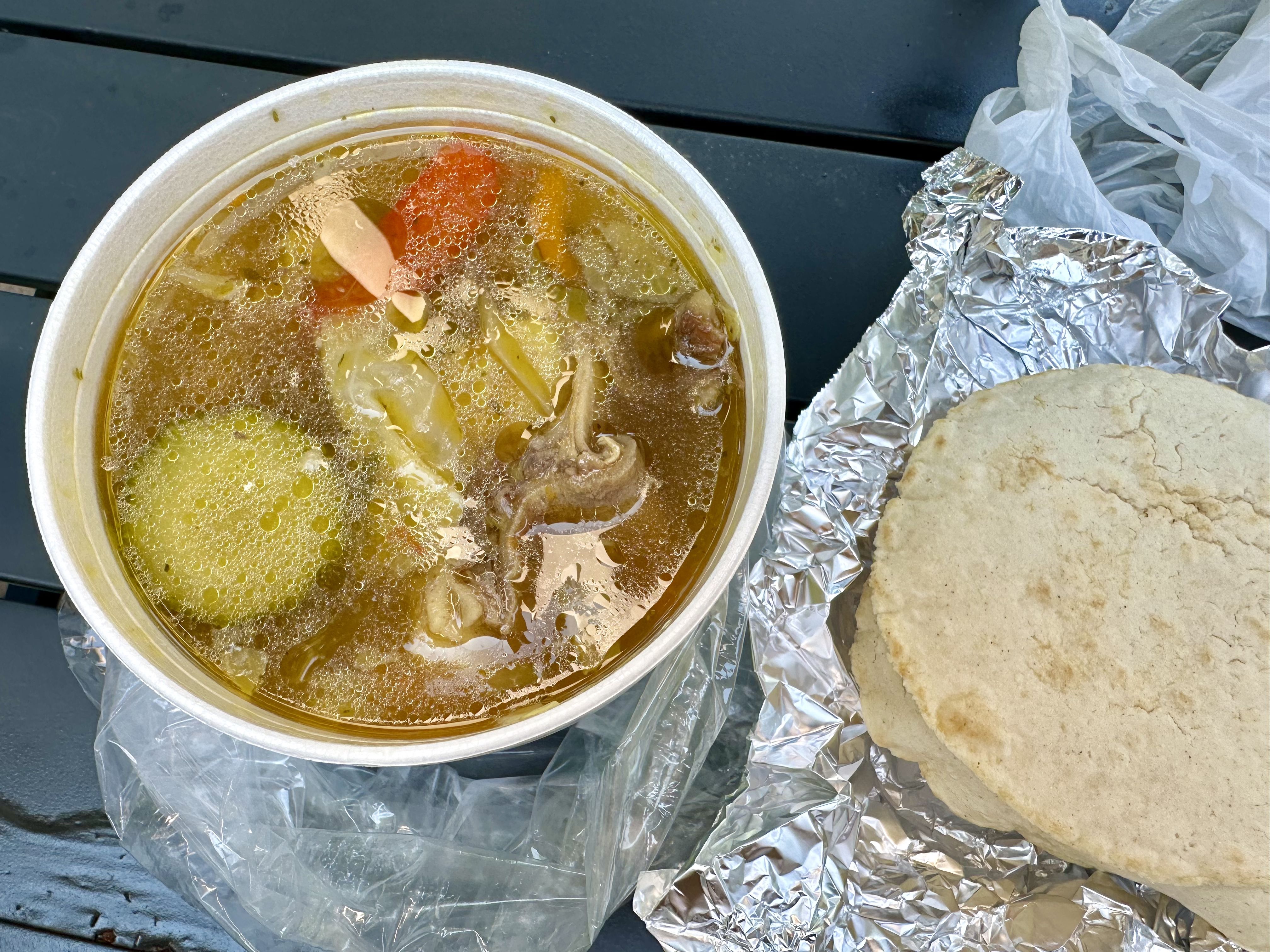 Photo shows a container of sopa de res served with tortillas and rice.