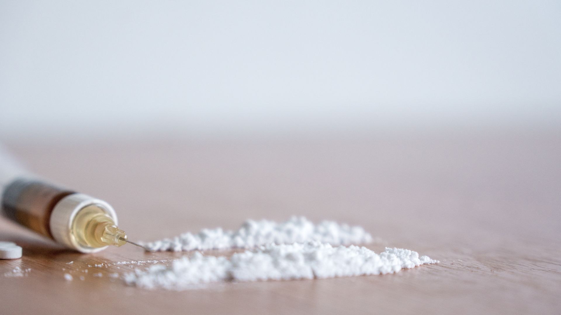 A syringe on a table with white heroin powder next to it