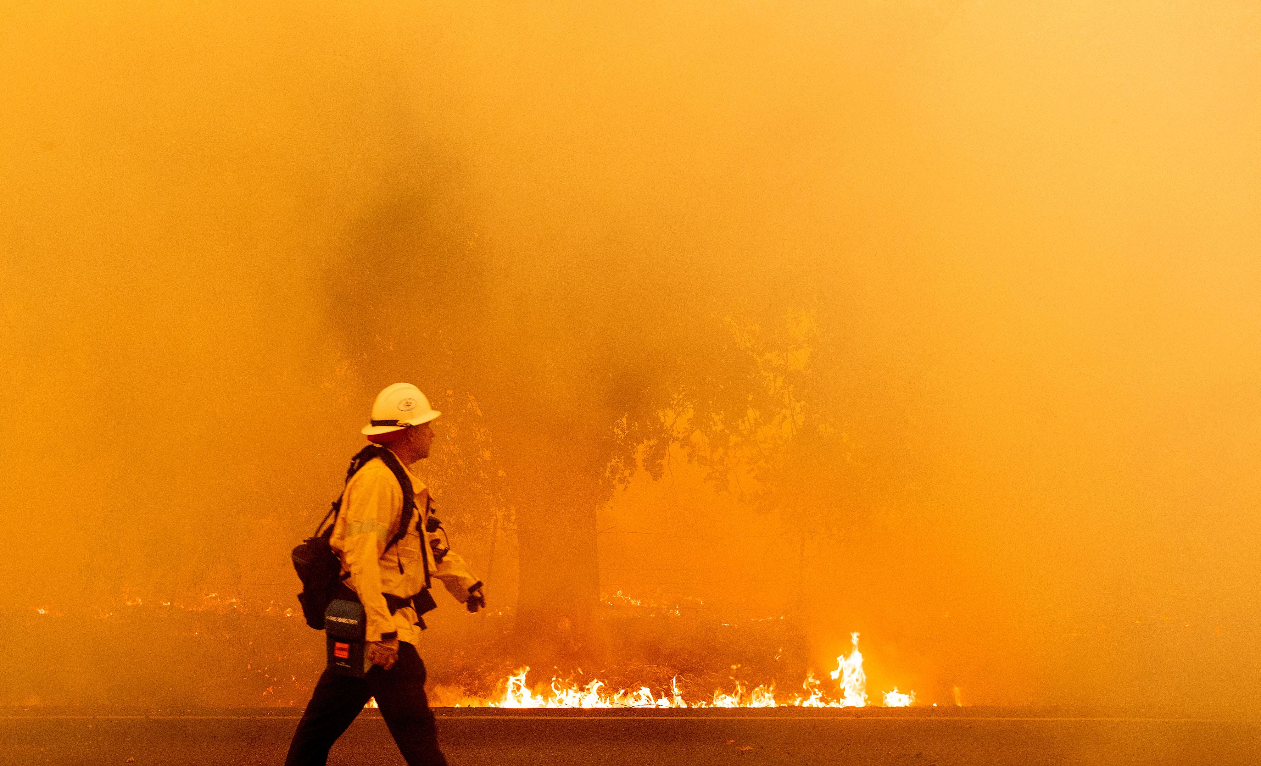 A Pacific Gas and Electric firefighter walks down a road as flames approach in Fairfield, California during the LNU Lightning Complex fire on August 19