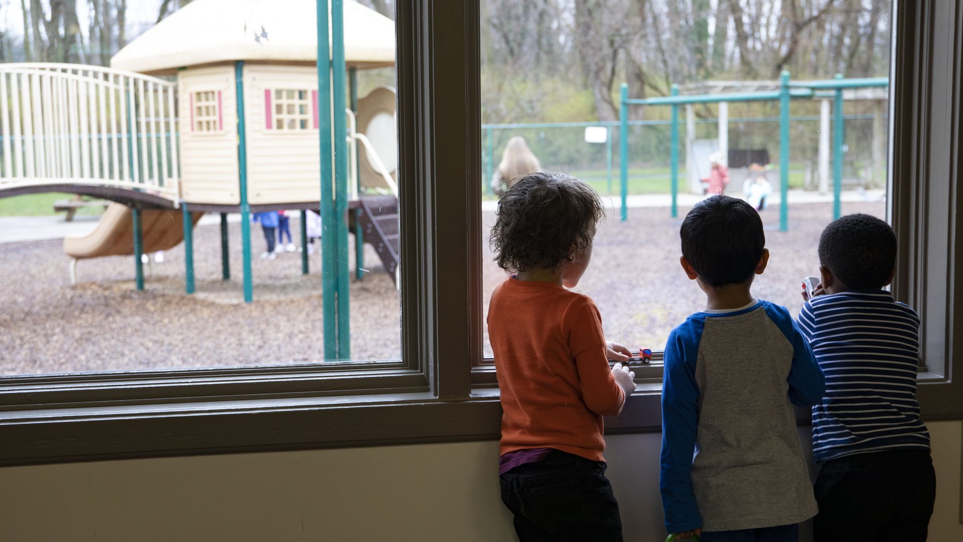A group of preschool-aged children look out the window at a playground