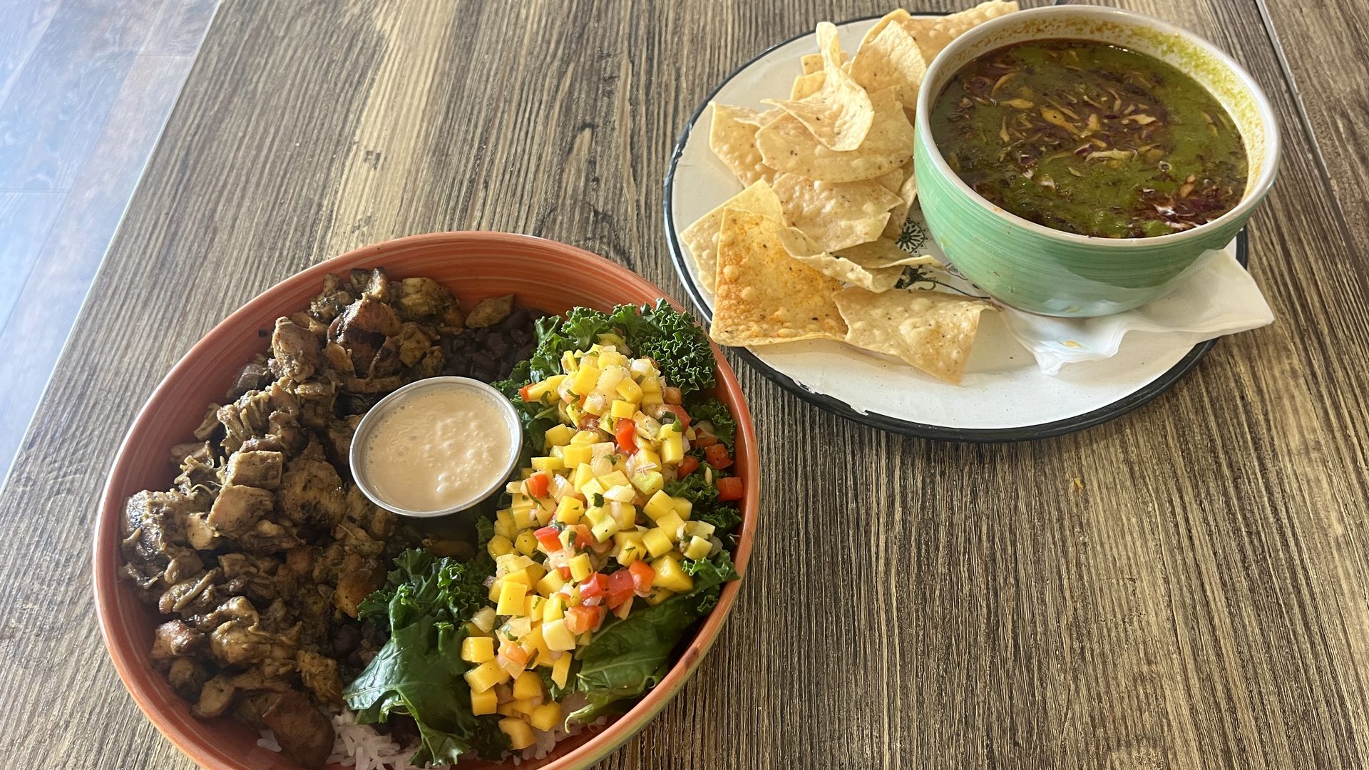 A chicken and rice bowl with mango salsa and a bowl of soup on a table at a restaurant. 