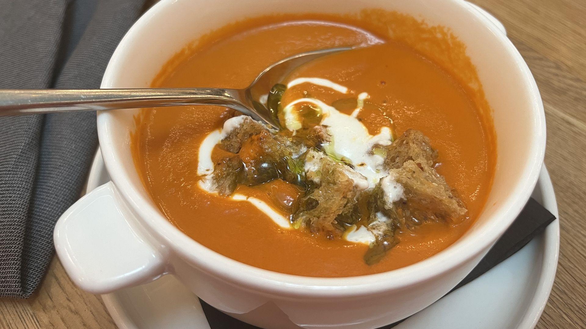 White bowl of tomato soup topped with croutons.