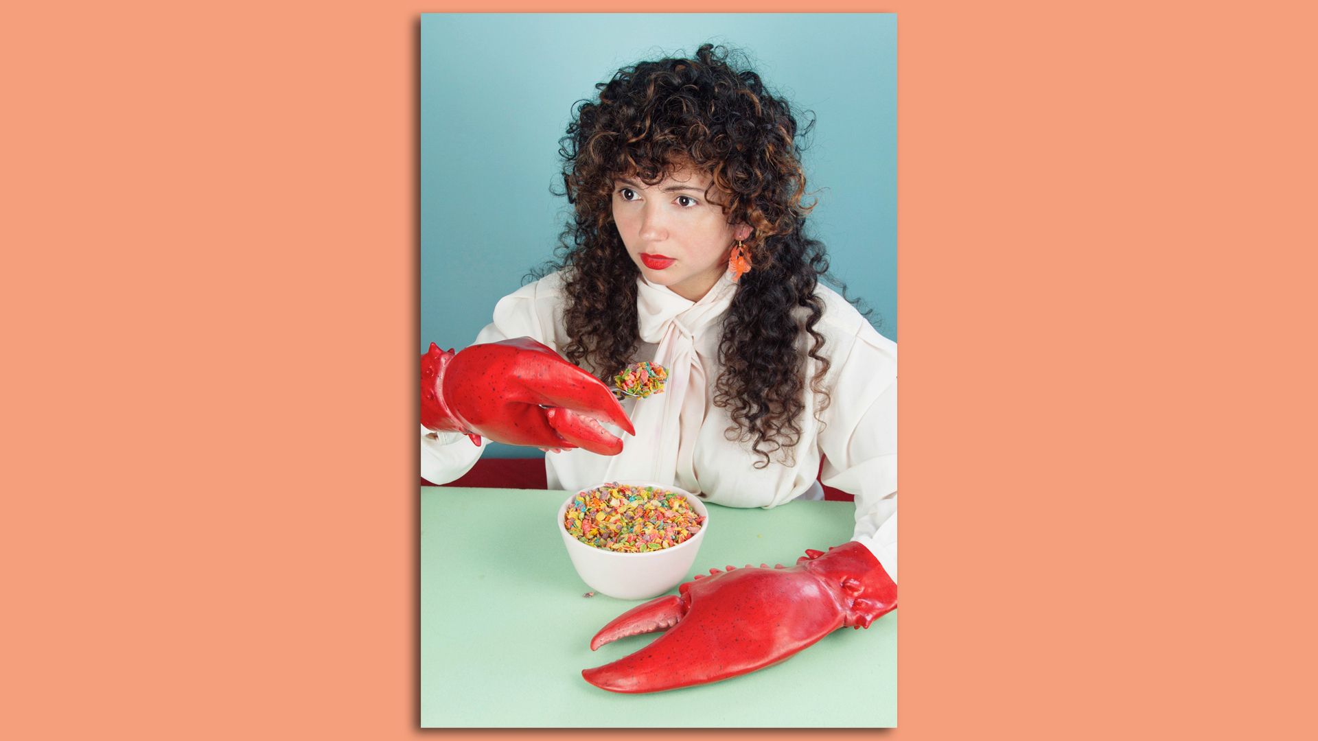 Stephanie Agudelo with lobster claws on her hands and a bowl of fruity pebbles cereal in front of her