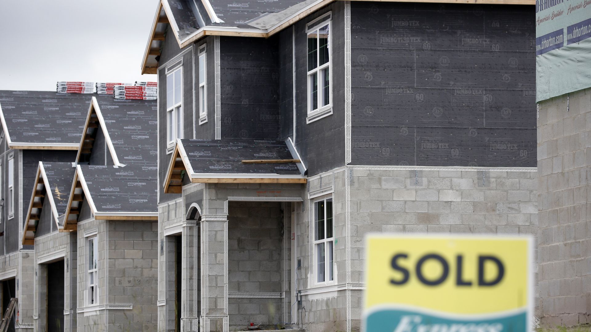 A luxury home under construction with a yellow and black "sold" sign.