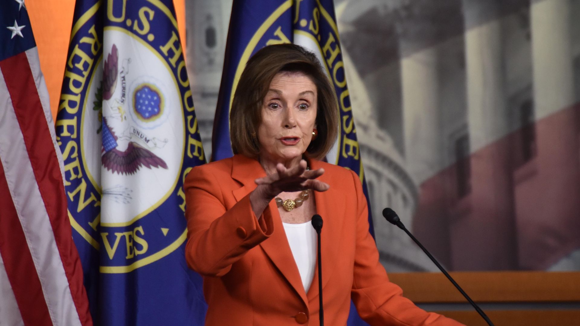House Speaker Nancy Pelosi stands in front of flags.