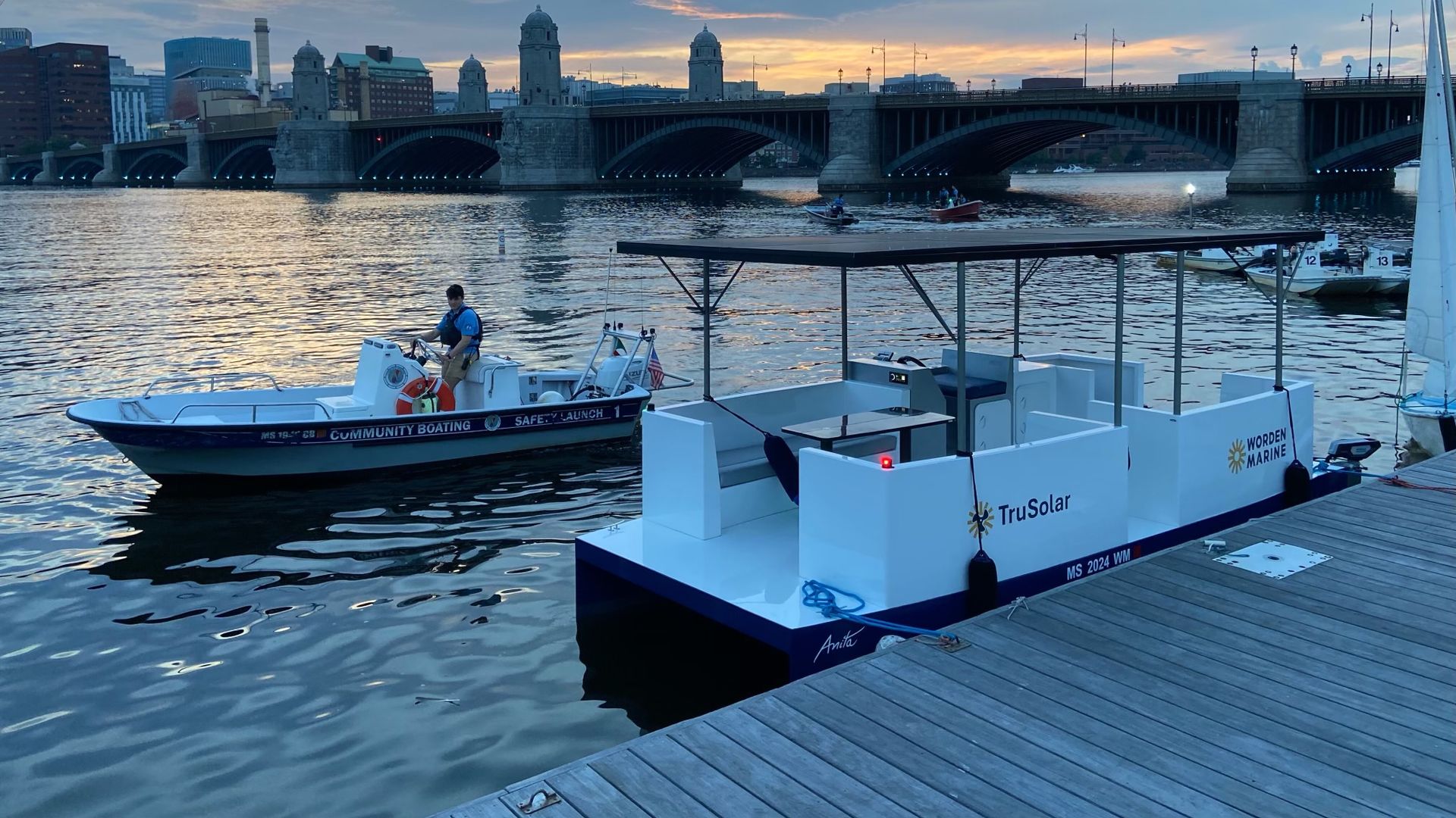 Worden Marine's 20-foot electric-solar vessel prototype is docked at Community Boating Inc's boathouse as a CBI worker in a safety boat looks on in Boston.