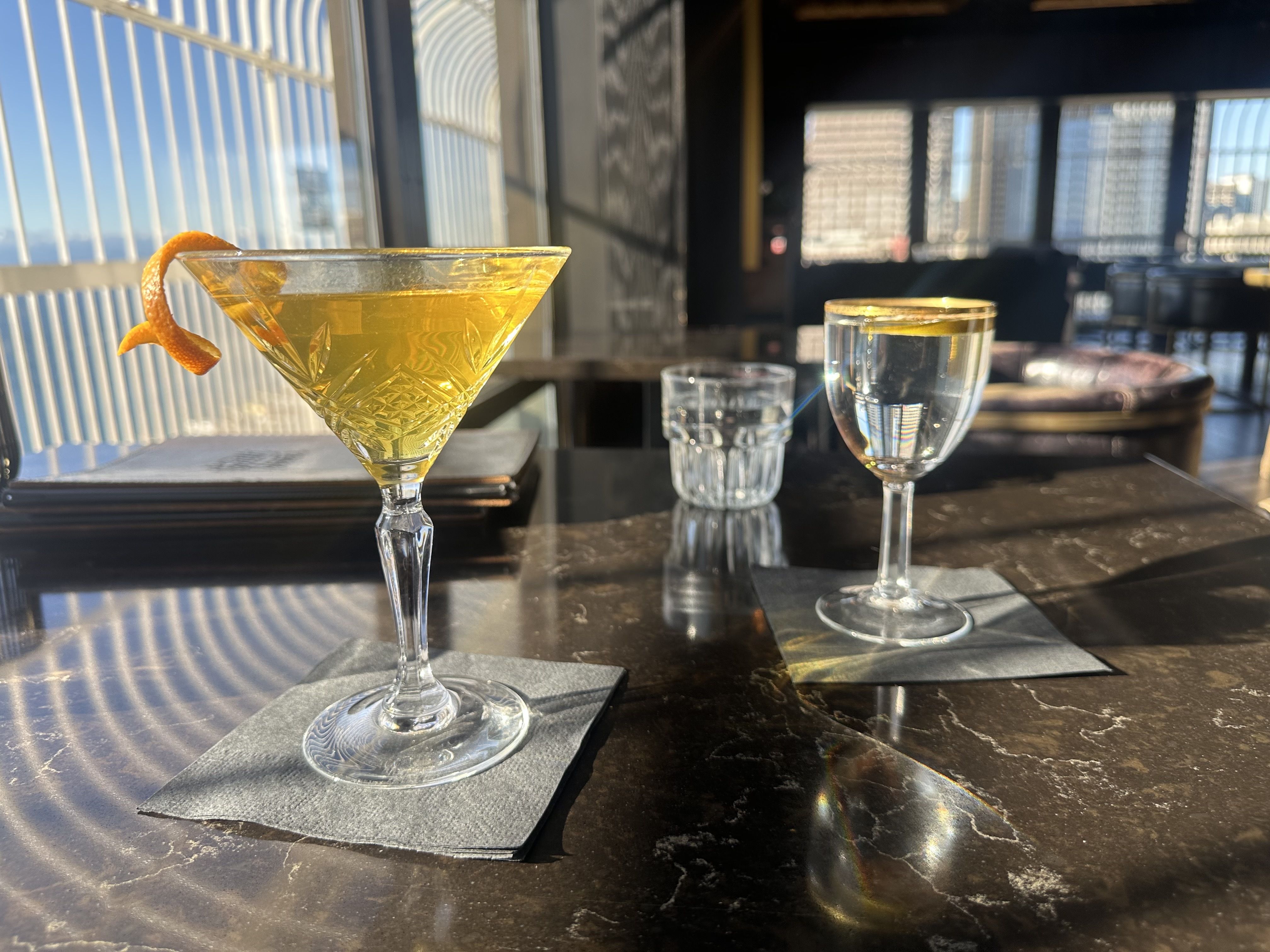 Cocktails at the Smith Tower on a table in front of long, glass windows. 