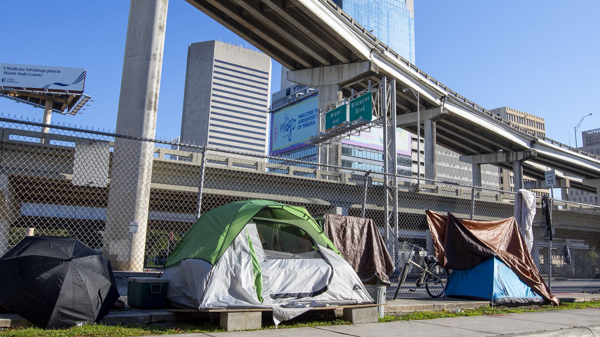A green tent is in the foreground. Behind it is a highway overpass and a Bank of Ameria building.