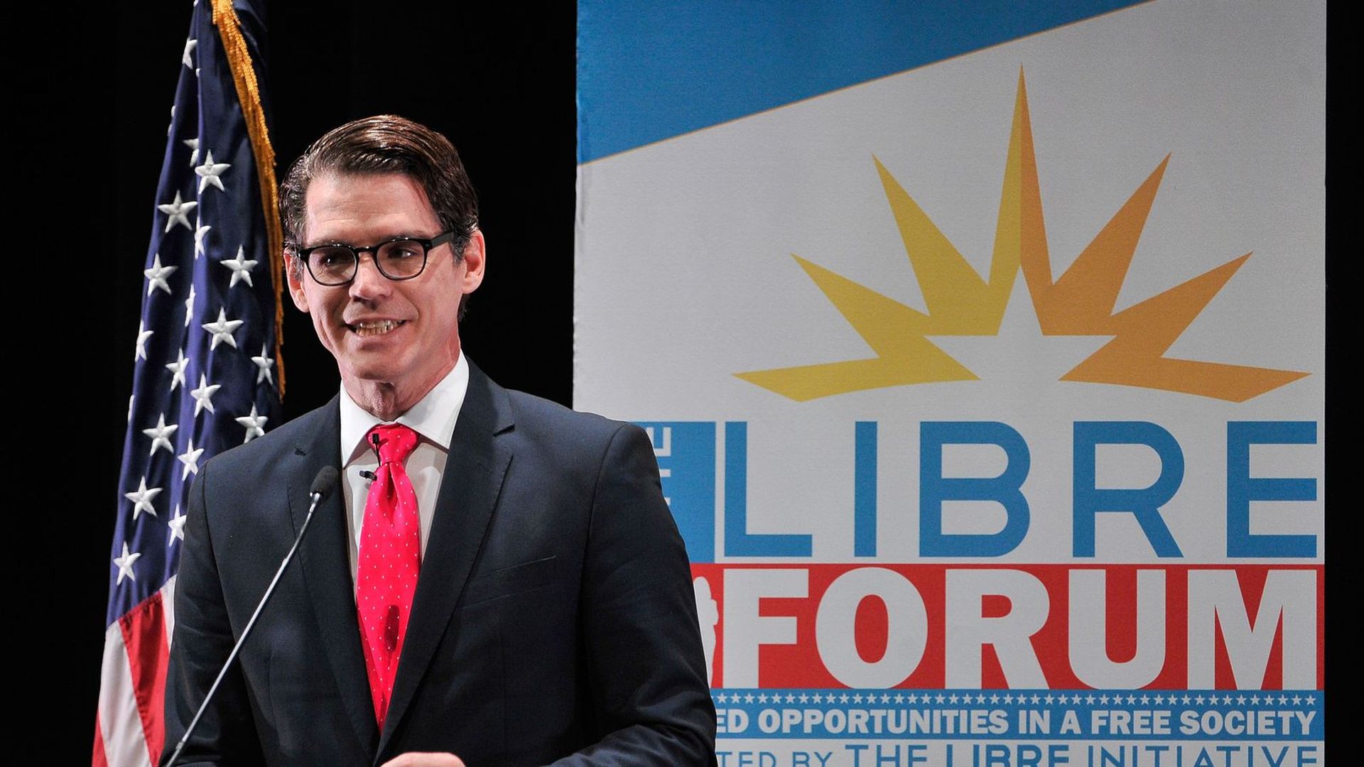 Daniel Garza stands in front of a microphone with a large sign behind him for the Libre initiative, which he heads