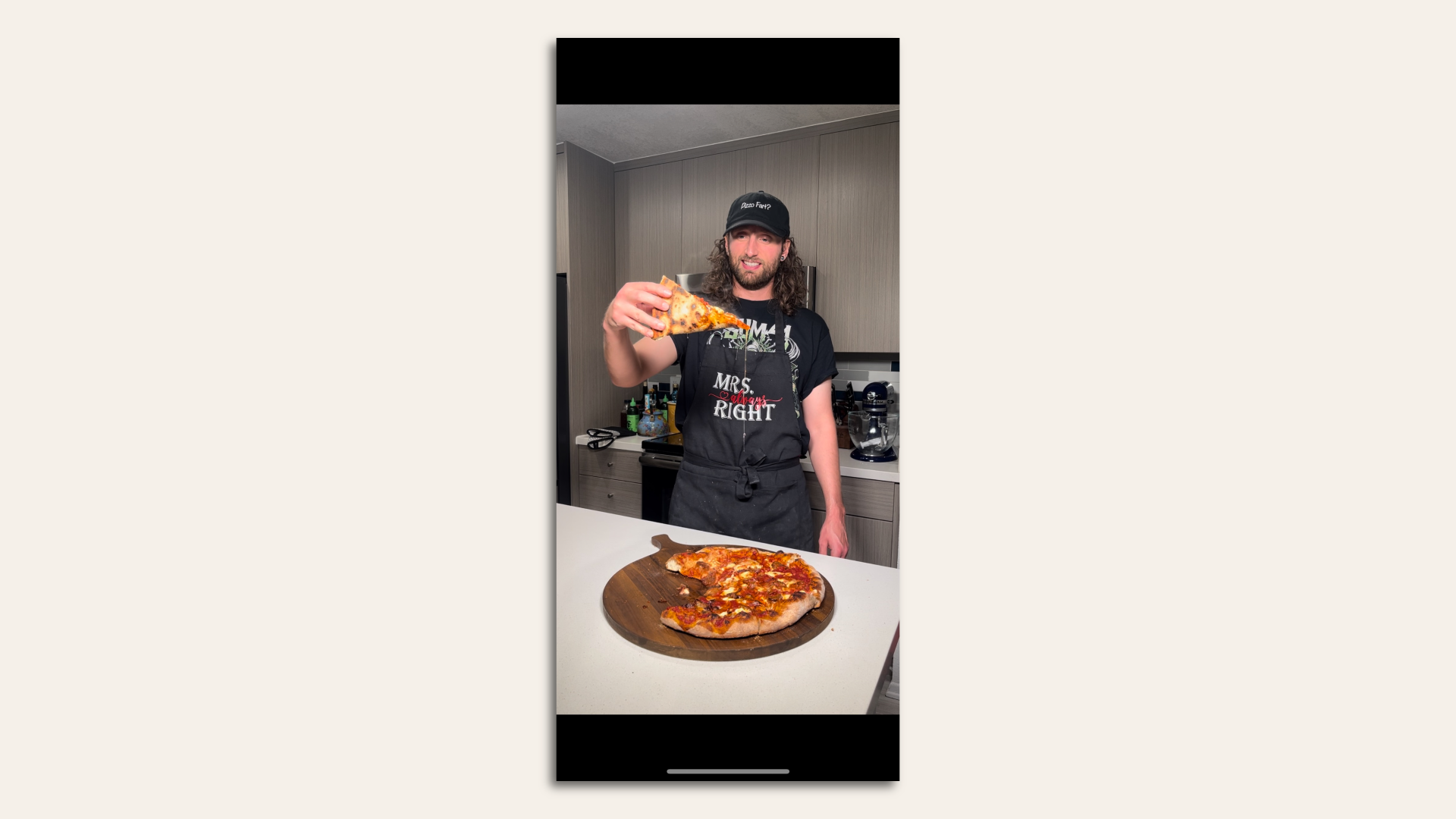A man hoists a slice of pizza, standing in front of a table with the rest of the pie.