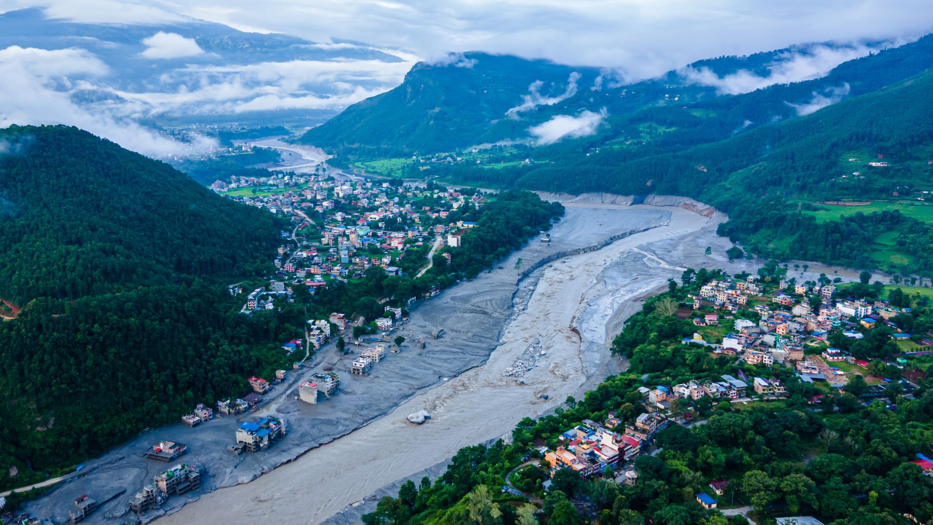 An aerial view of flood damage along the Bhotekoshi River in Nuwakot, with debris surrounding buildings and roads near the river.