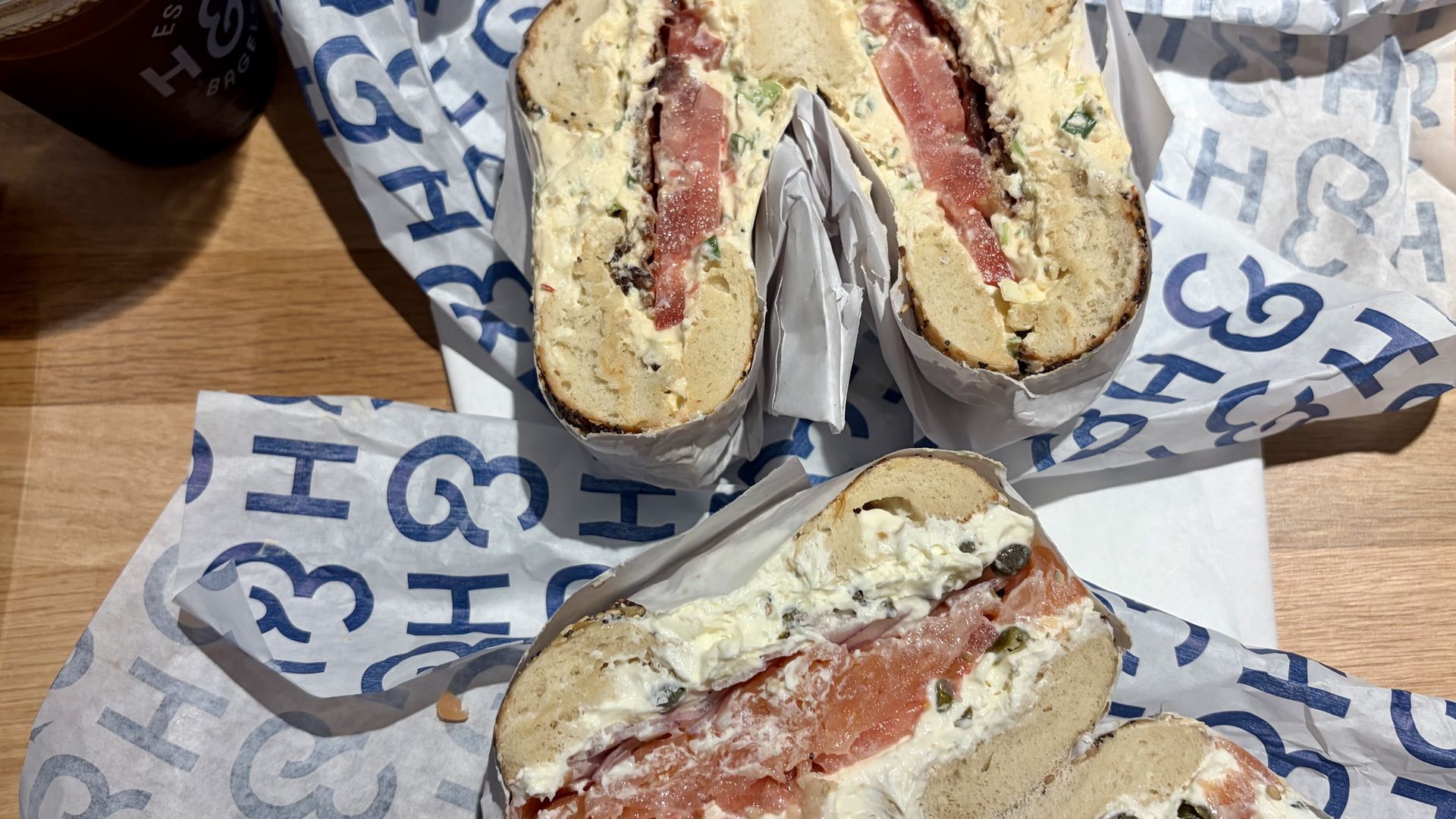Three bagel halves filled with cream cheese and smoked salmon, red onion, and herbs on a wooden table. 