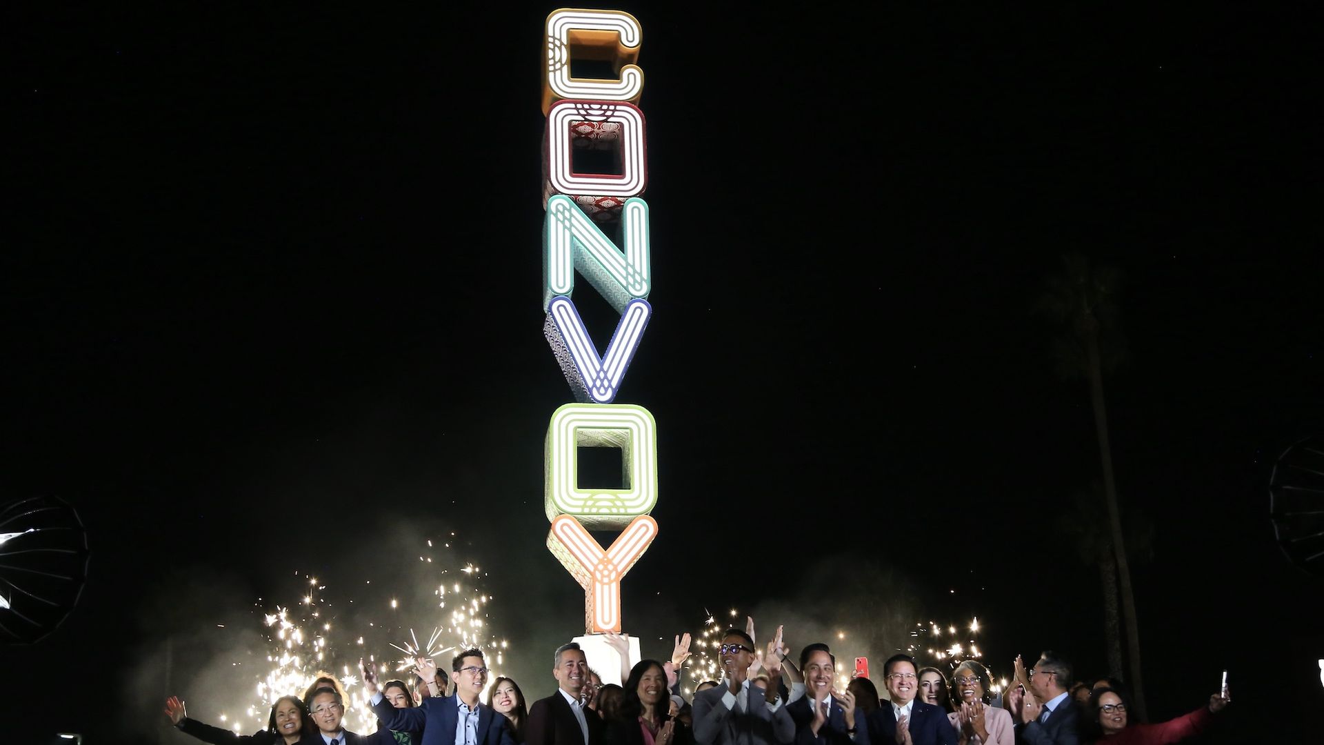 A large rainbow-colored sign that says "CONVOY" is lit up with people cheering below.
