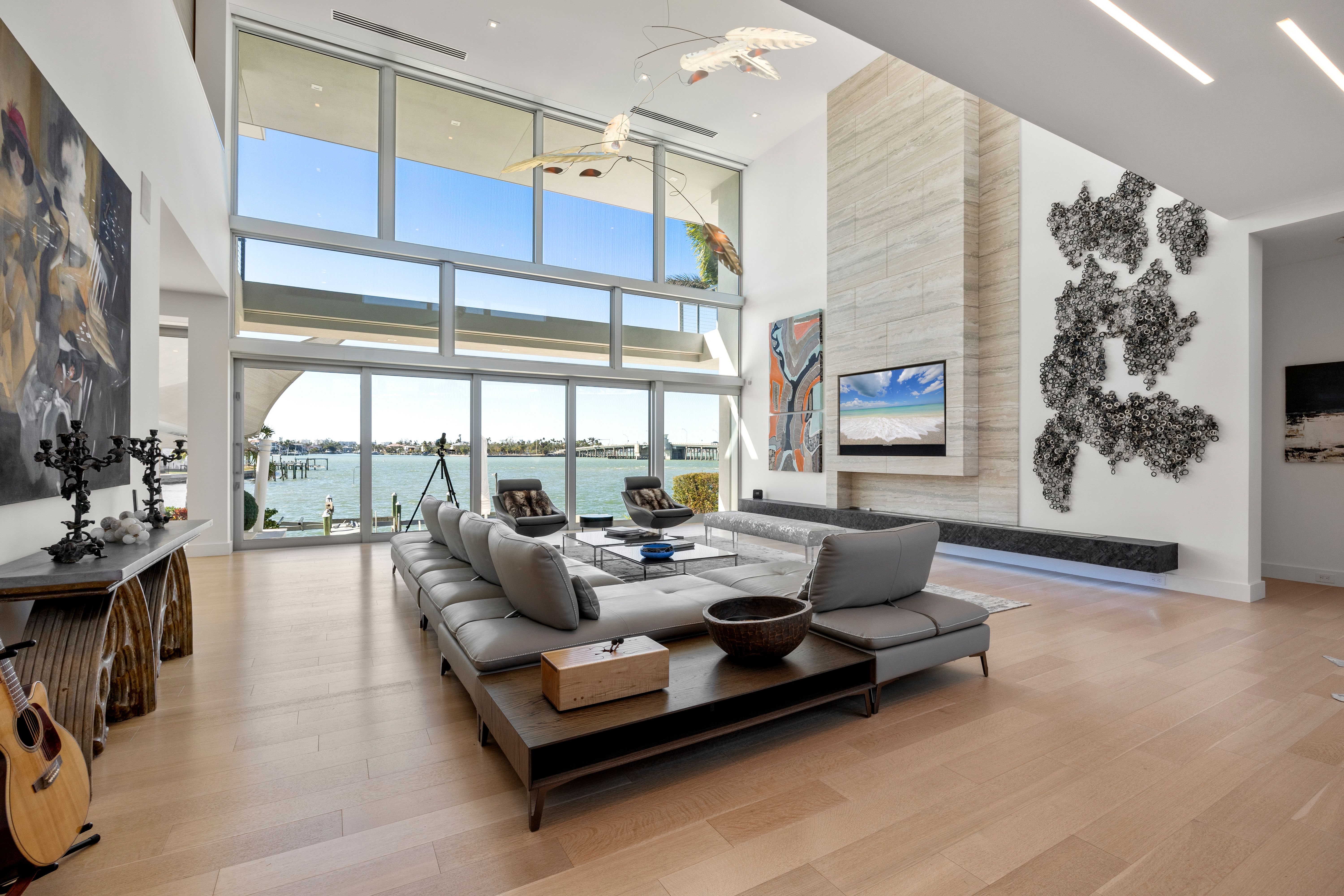 A living room with a gray modern sectional and wooden tables overlooking a back patio with a view of the water.