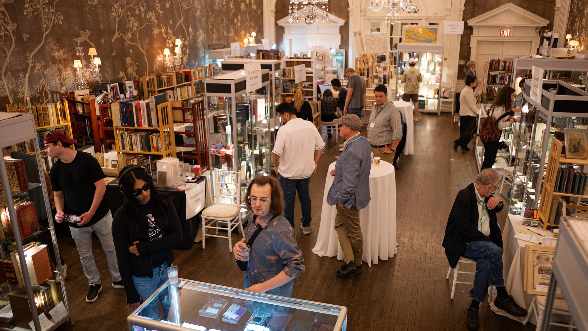 A room with chandeliers filled with people browsing rare books