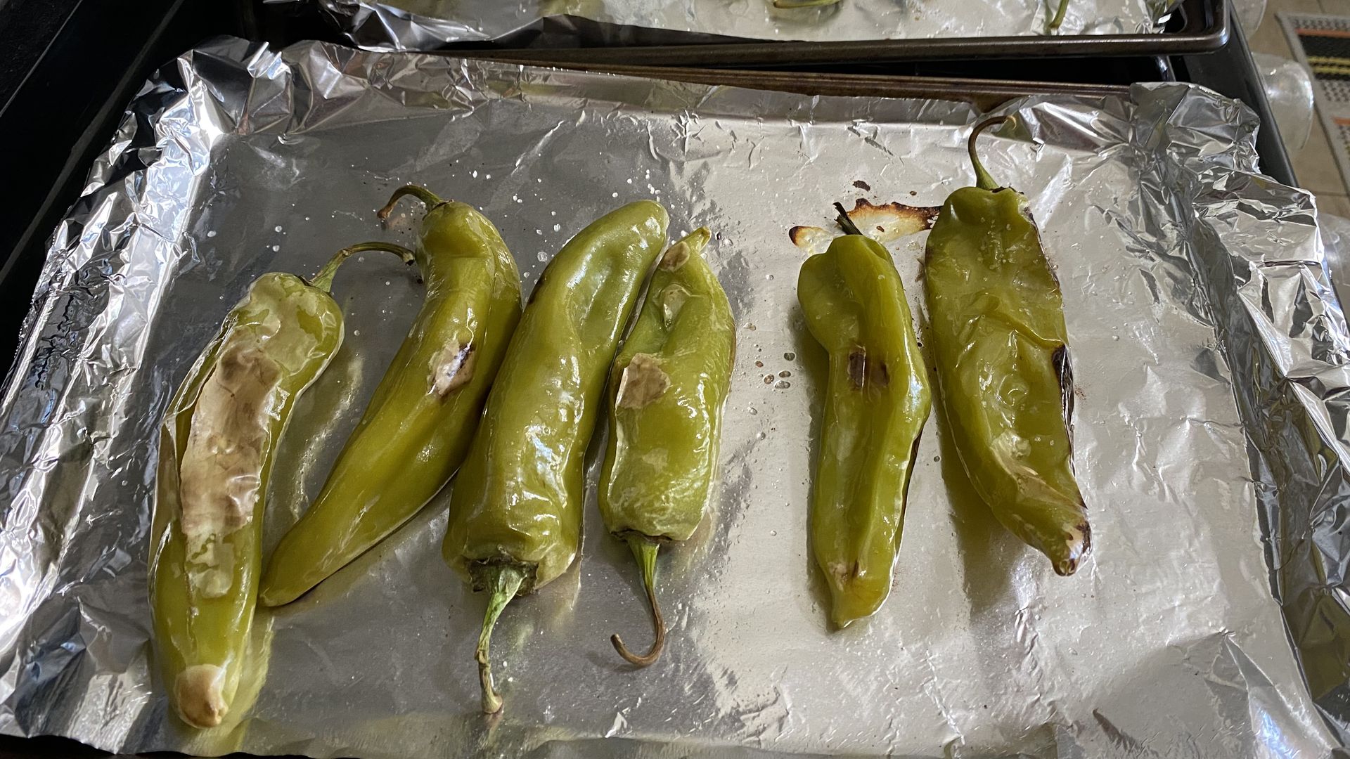 Roasted hatch green chiles lined up on two foil lined baking sheets
