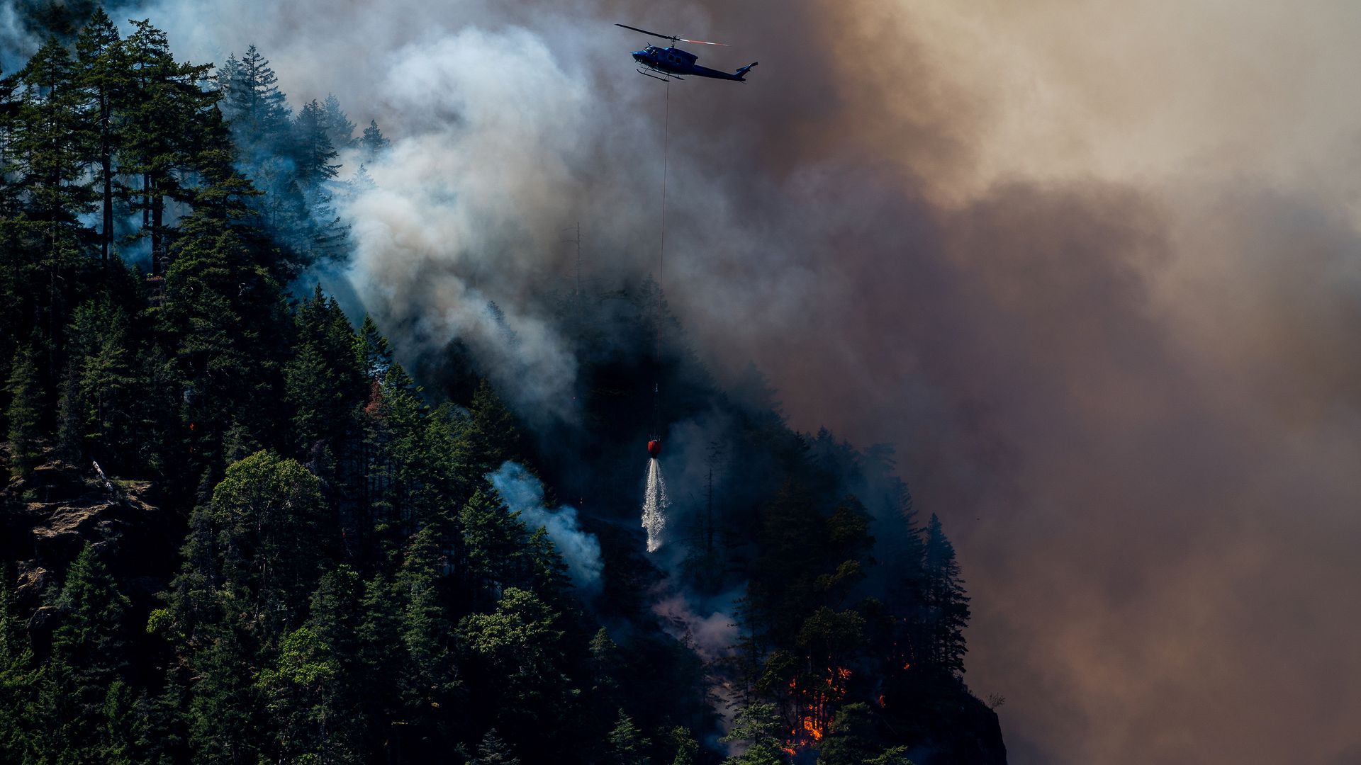 A helicopter waterbomber drops water onto the Cameron Bluffs wildfire near Port Alberni, British Columbia, Canada, on Tuesday, June 6, 2023. 