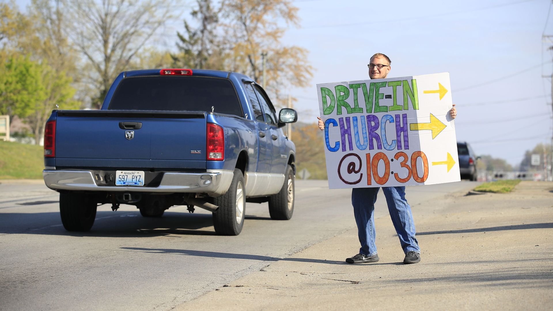 Man holding a sign on the road about a drive-in church