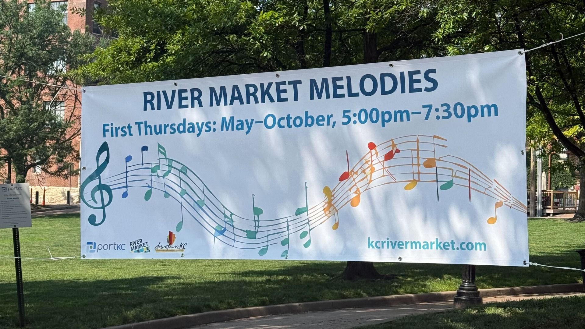 A sign advertises the River Market Melodies concert series showing dates, times, and graphic musical notes.