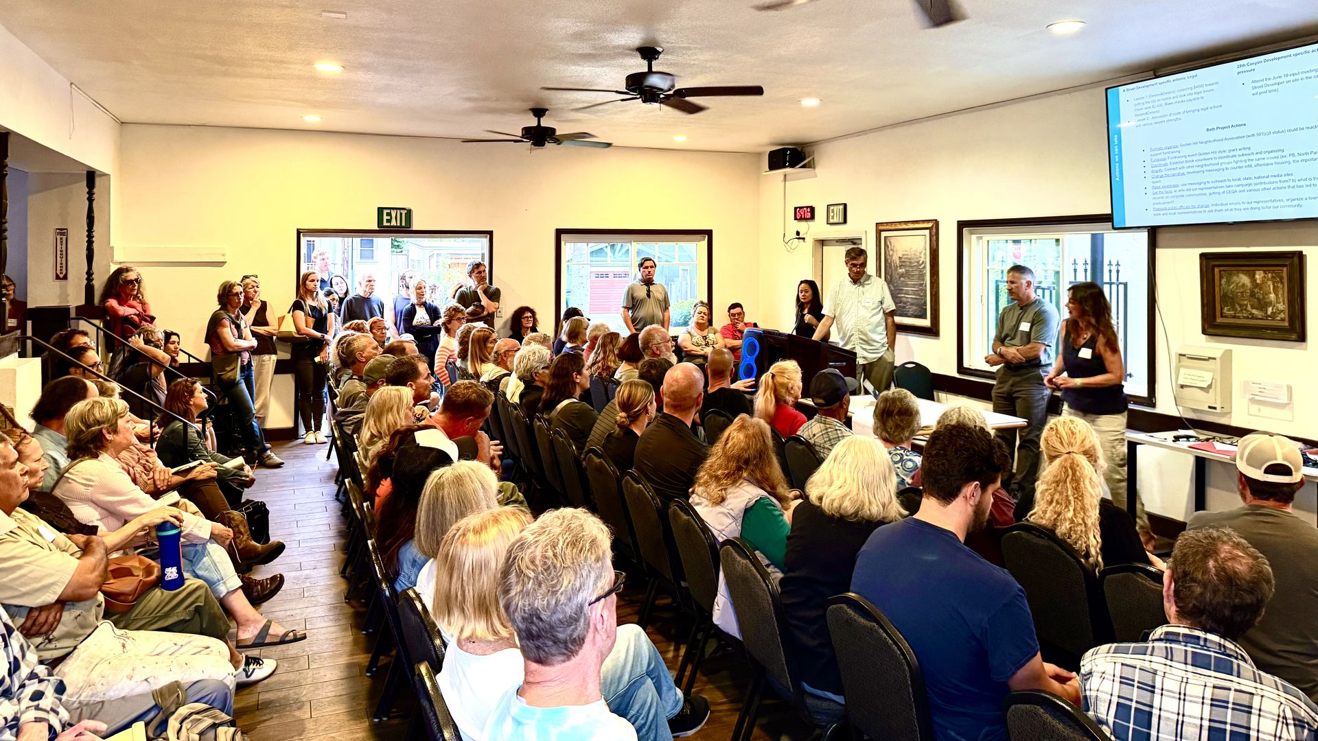 A room of people watching two speakers deliver a power point presentation