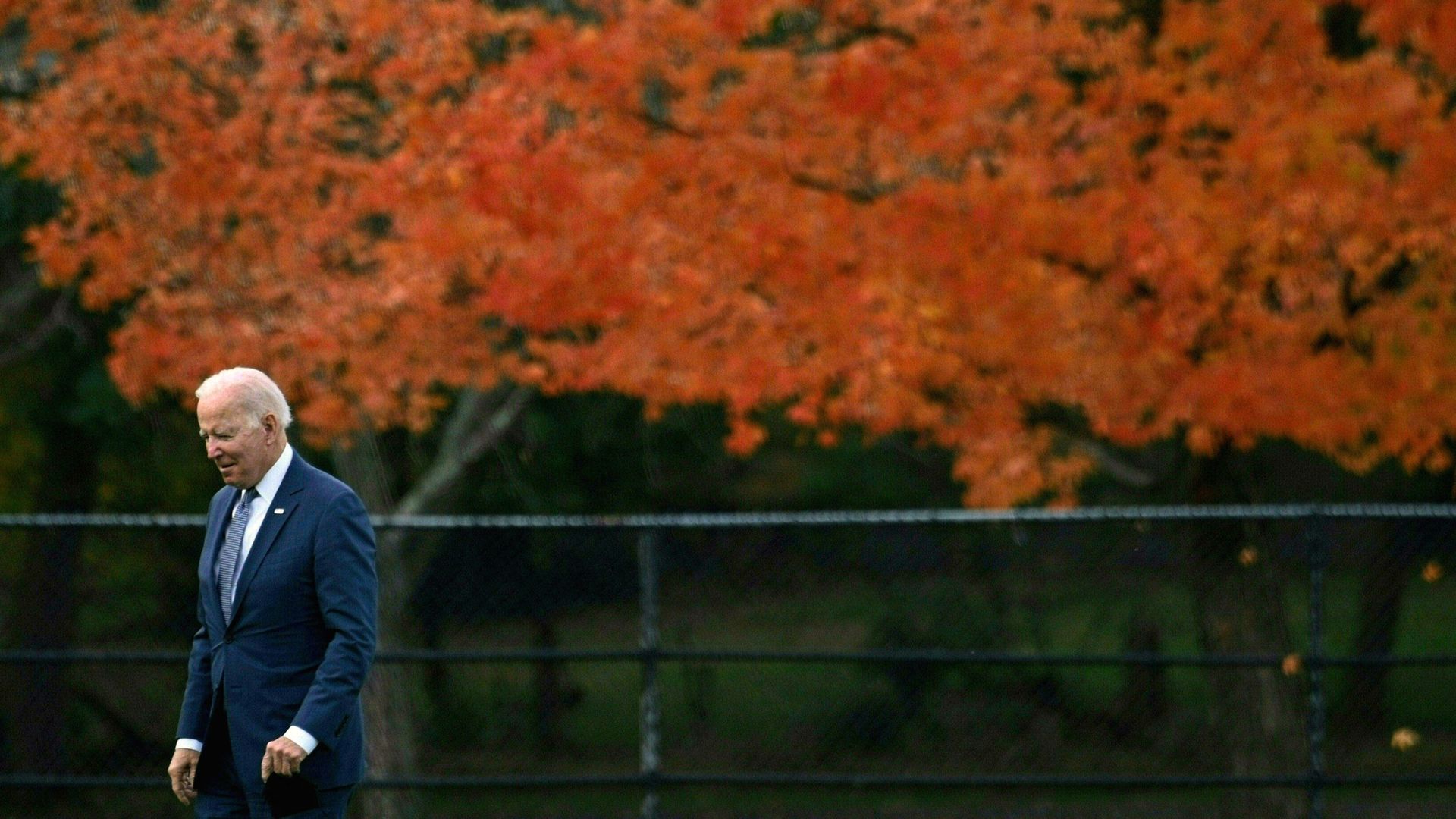President Biden is seen walking against a backdrop of bright orange fall leaves.