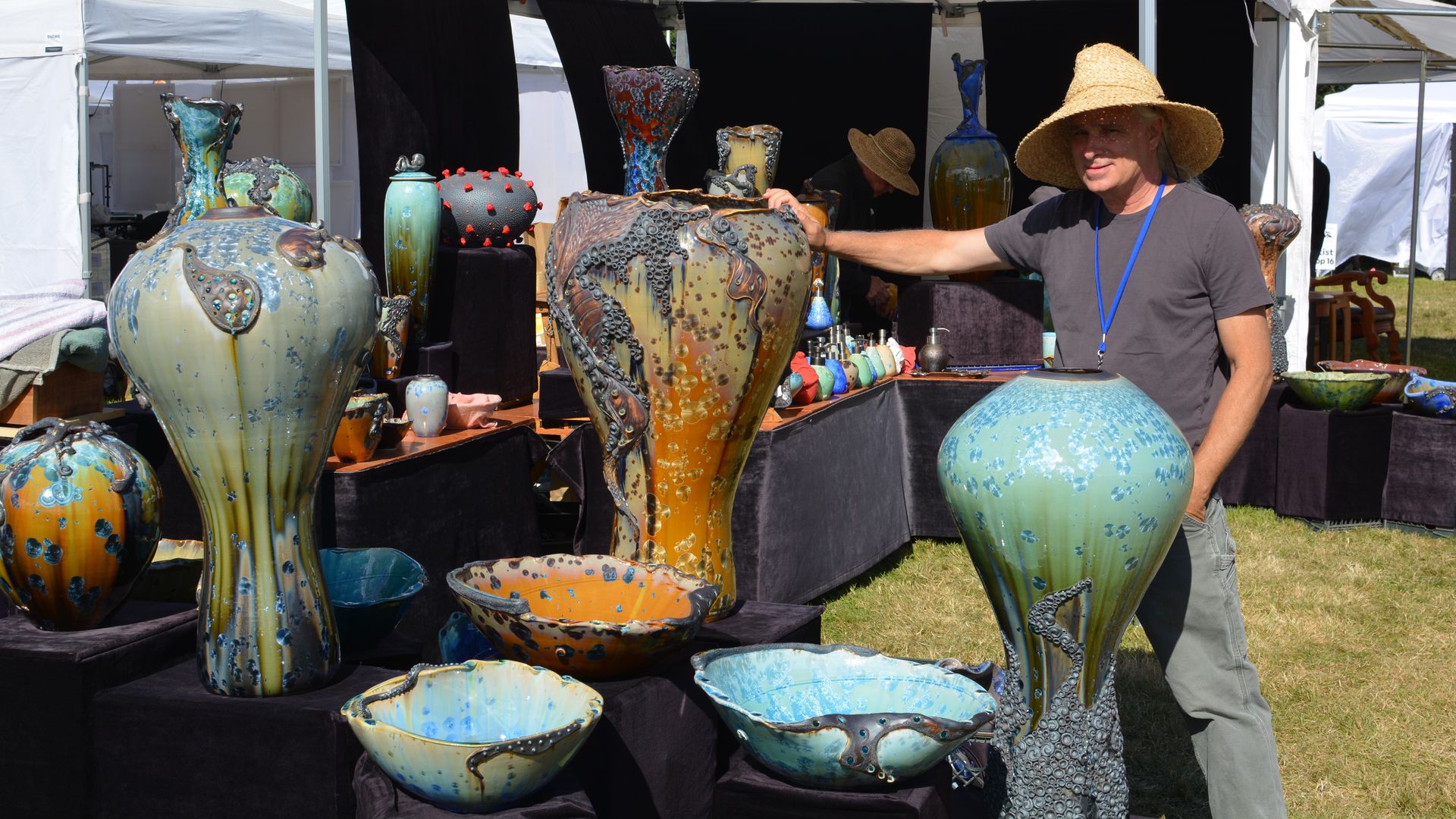 A man wearing a straw hat stands in front of tall turquoise pots.