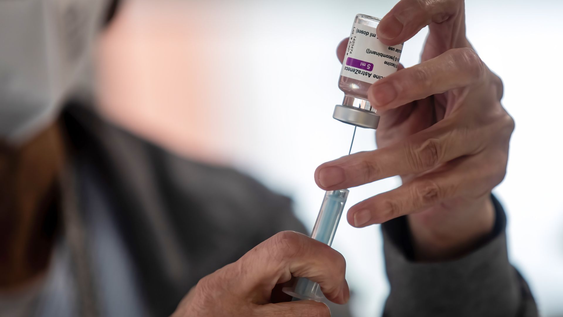 A hand holding a vial of the AstraZeneca vaccine along with a syringe.