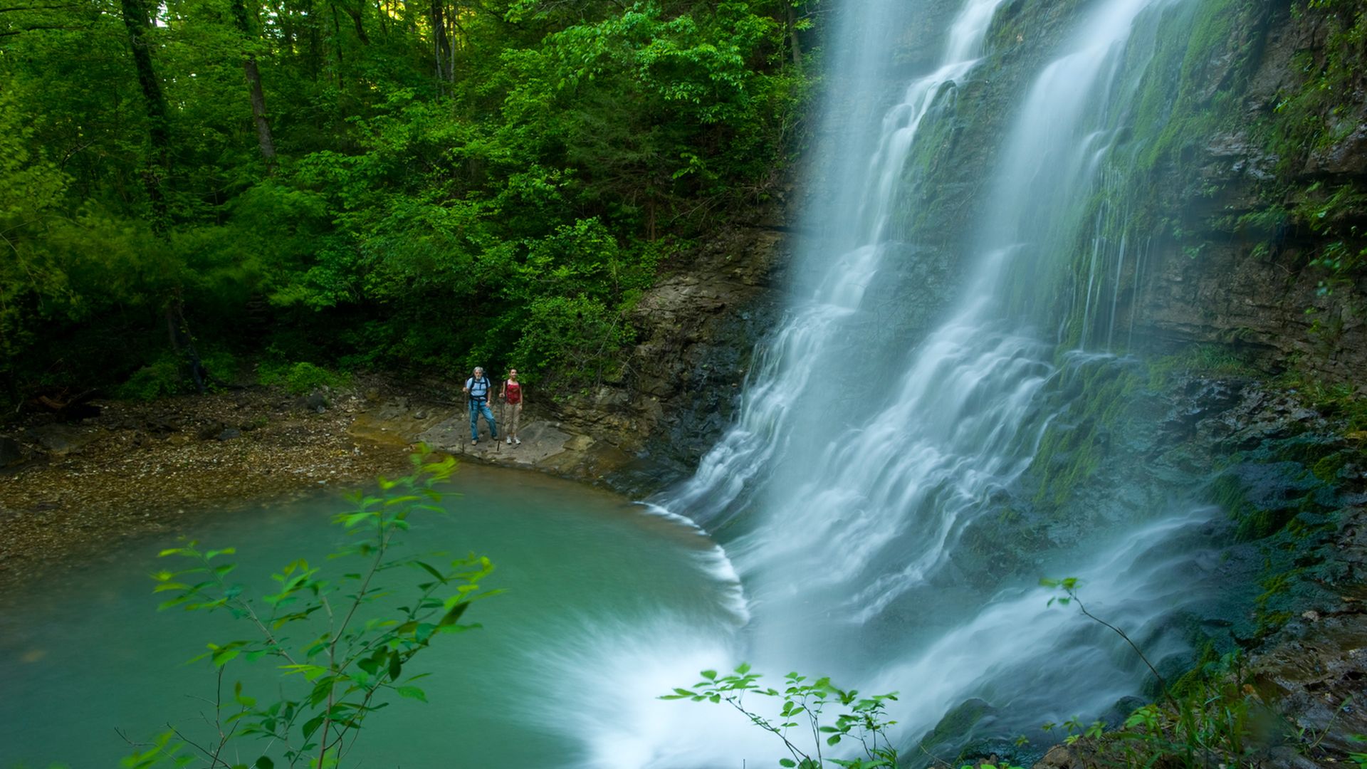 A photo of two people looking at a tall waterfall. 