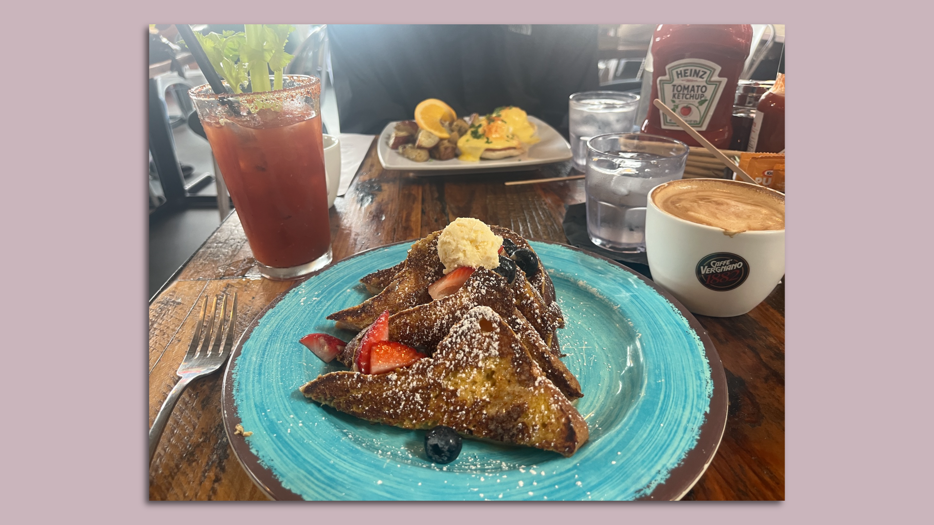 A plate of french toast, eggs Benedict, a bloody mary and a coffee on a restaurant table.