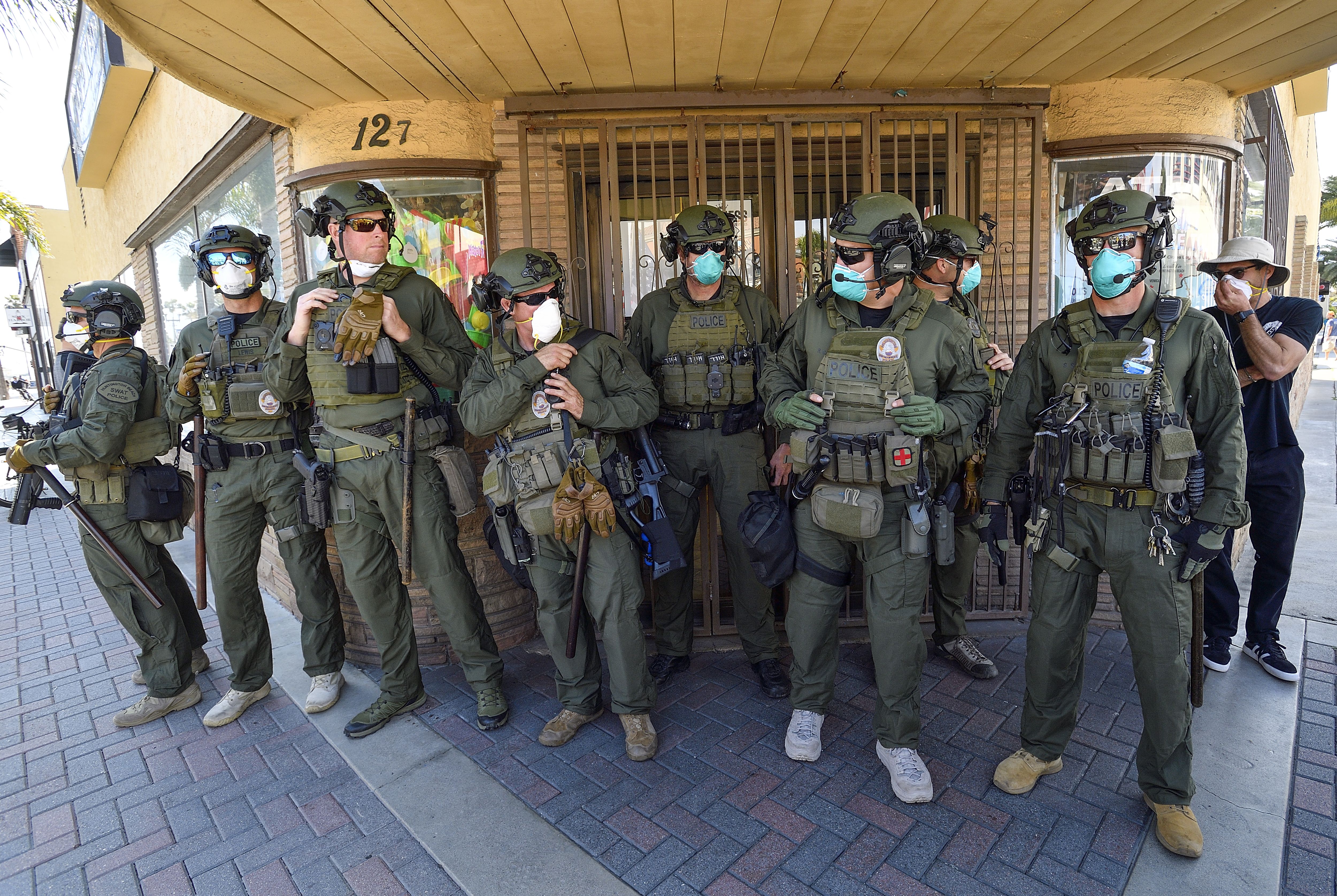 In this image, a line of police officers stand outside wearing face masks