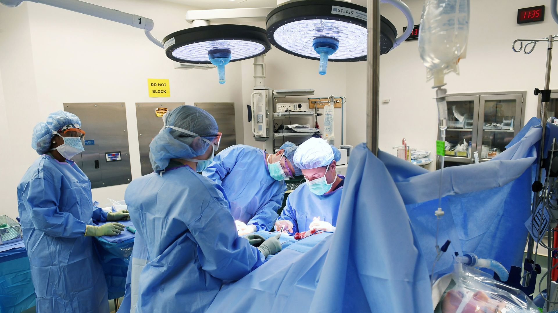 Doctors and nurses in blue gowns and masks operate around a surgical table in an operating room.