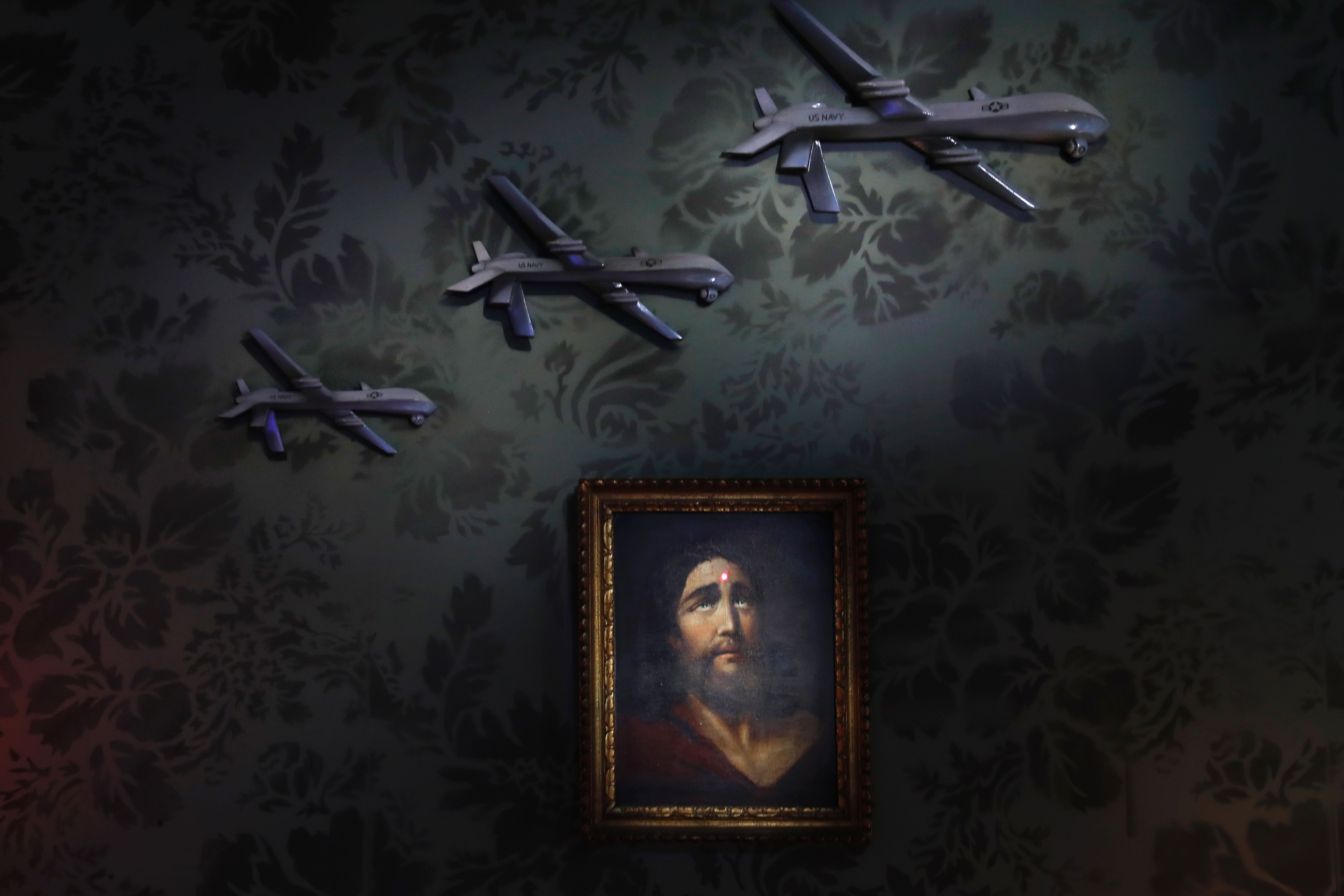 A painting depicting Jesus Christ with a weapon's laser red dot on his forehead and US military drones is seen in the lobby inside street artist Banksy's newly opened Walled Off hotel in the Israeli occupied West Bank town of Bethlehem, on March 15, 2017.