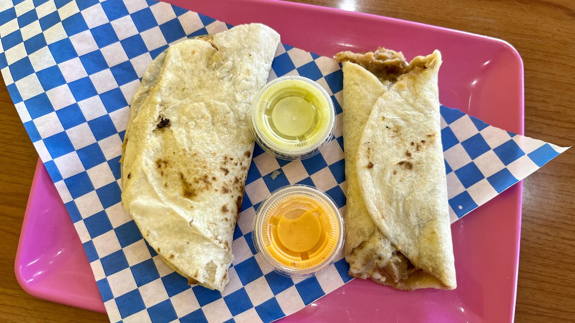 Vegan breakfast tacos with red and green salsas on a bright pink plate with a blue and white checkered napkin.