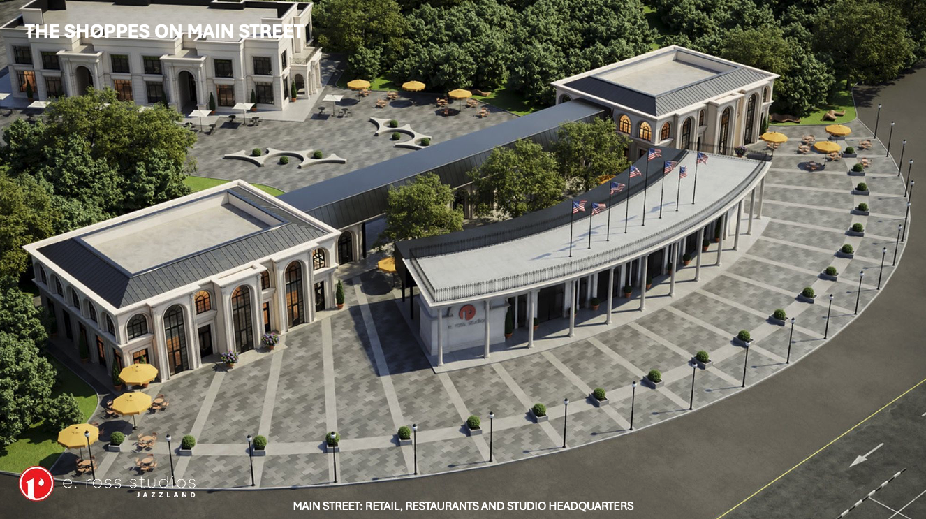 An aerial view of a curved, white neoclassical shopping plaza labeled "The Shoppes on Main Street" featuring a glass-roofed arcade, flagpoles, outdoor seating, and a wide tiled plaza with lamps.