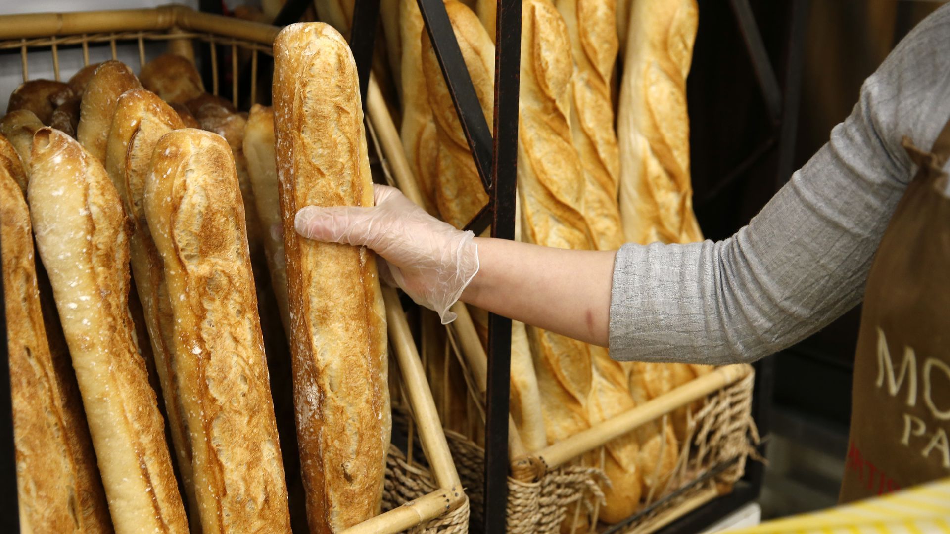 A baker holds a freshly baked baguette inside a bakery in Paris.