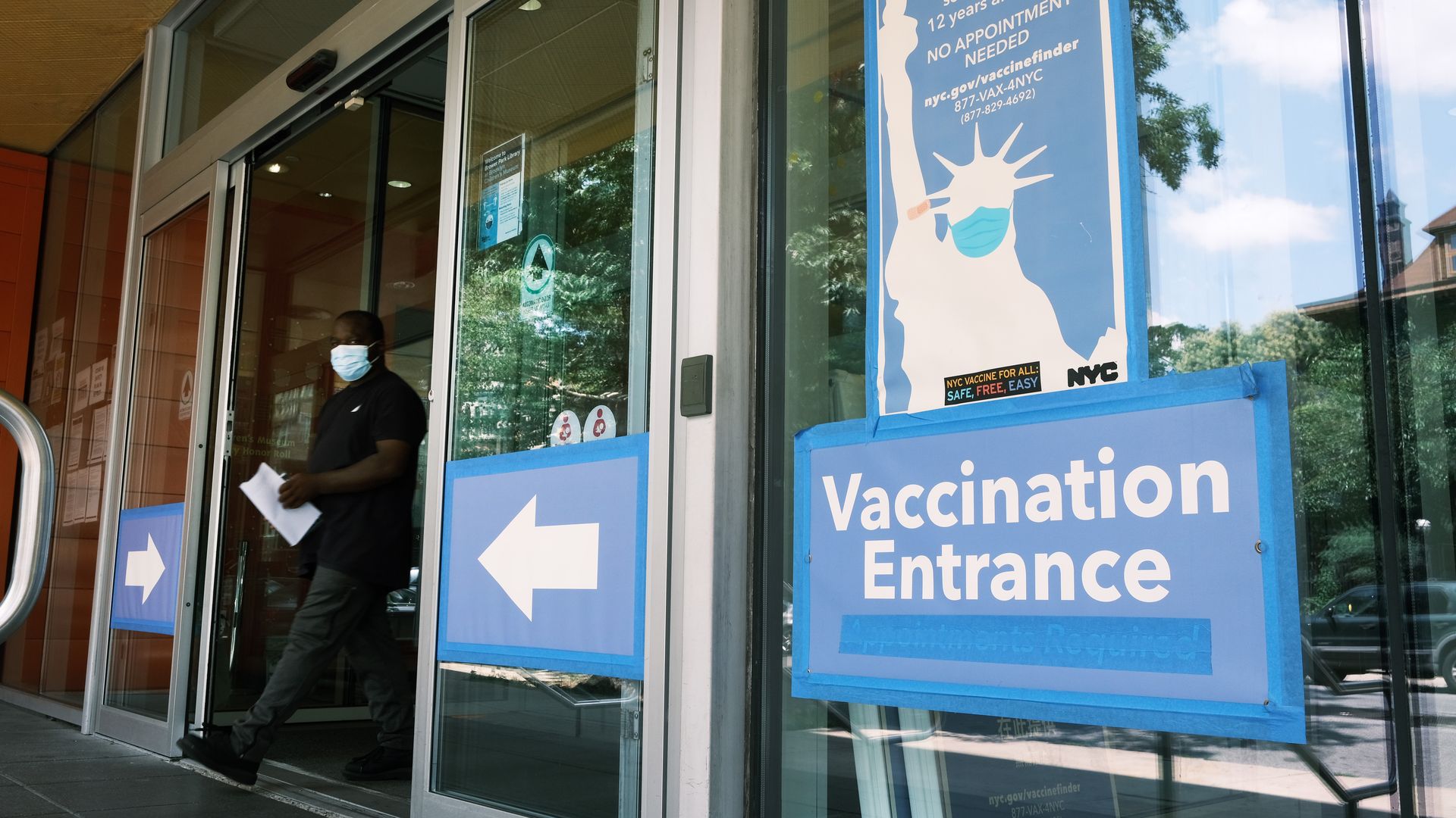 Photo of a sign that says "Vaccination entrance" and points to doors that are open as a man walks out