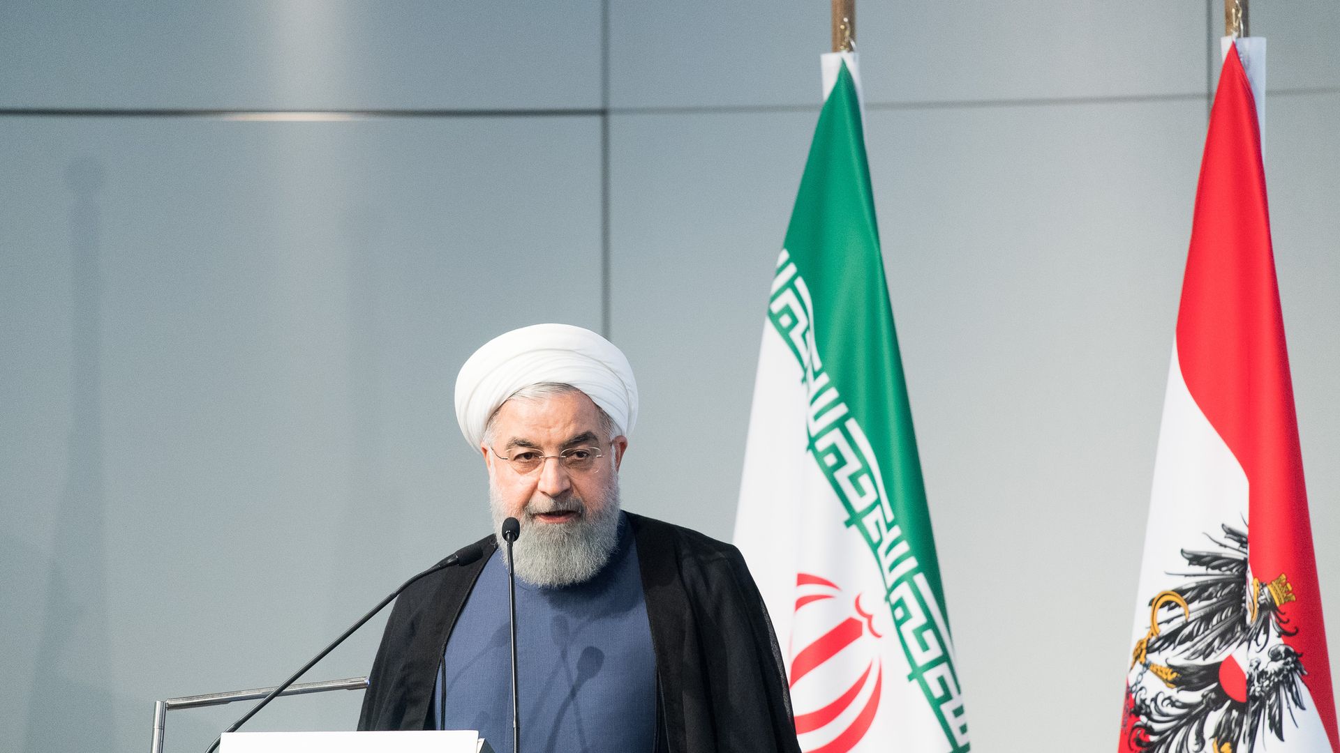 Iranian President Hassan Rouhani speaking in front of two flags.