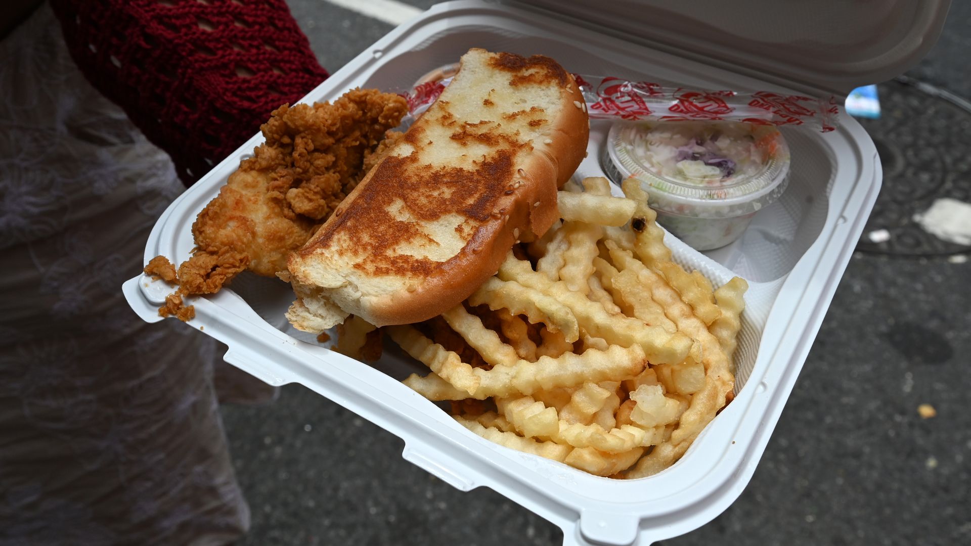 A takeout clamshell is open to reveal a Raising Cane's meal, including fries, toast, slaw and chicken.